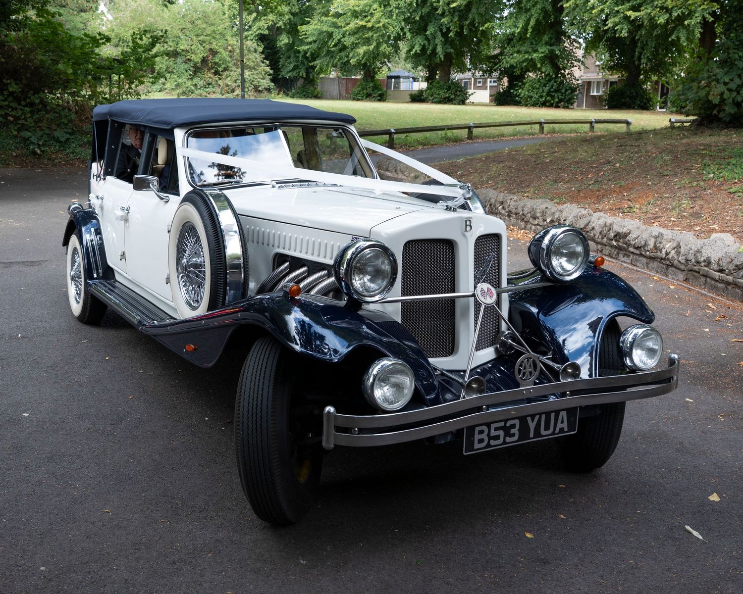 Classic vintage white Beauford wedding car parked on a tree-lined street.