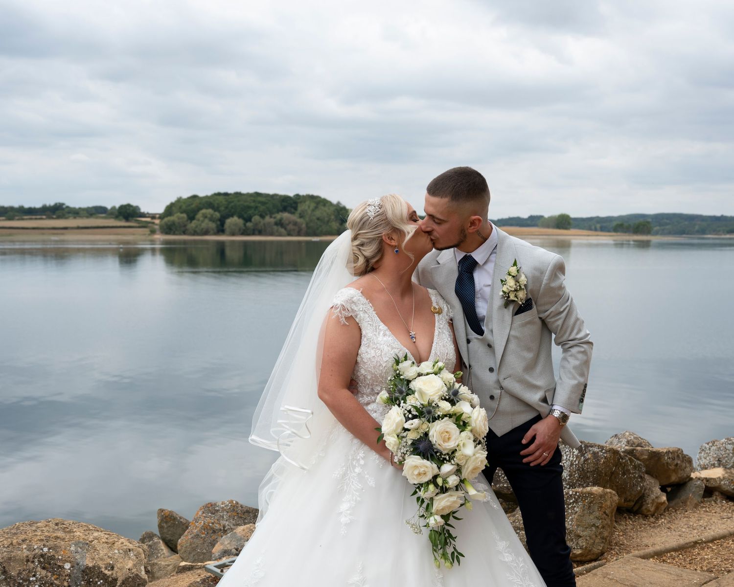 A couple shares romantic moments by a lakeside during their wedding photoshoot.