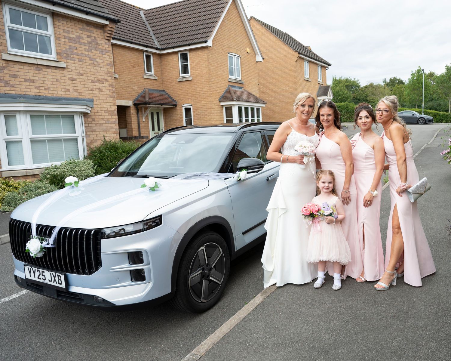 Wedding group photos with bridesmaids in pink dresses posing next to a silver luxury vehicle.