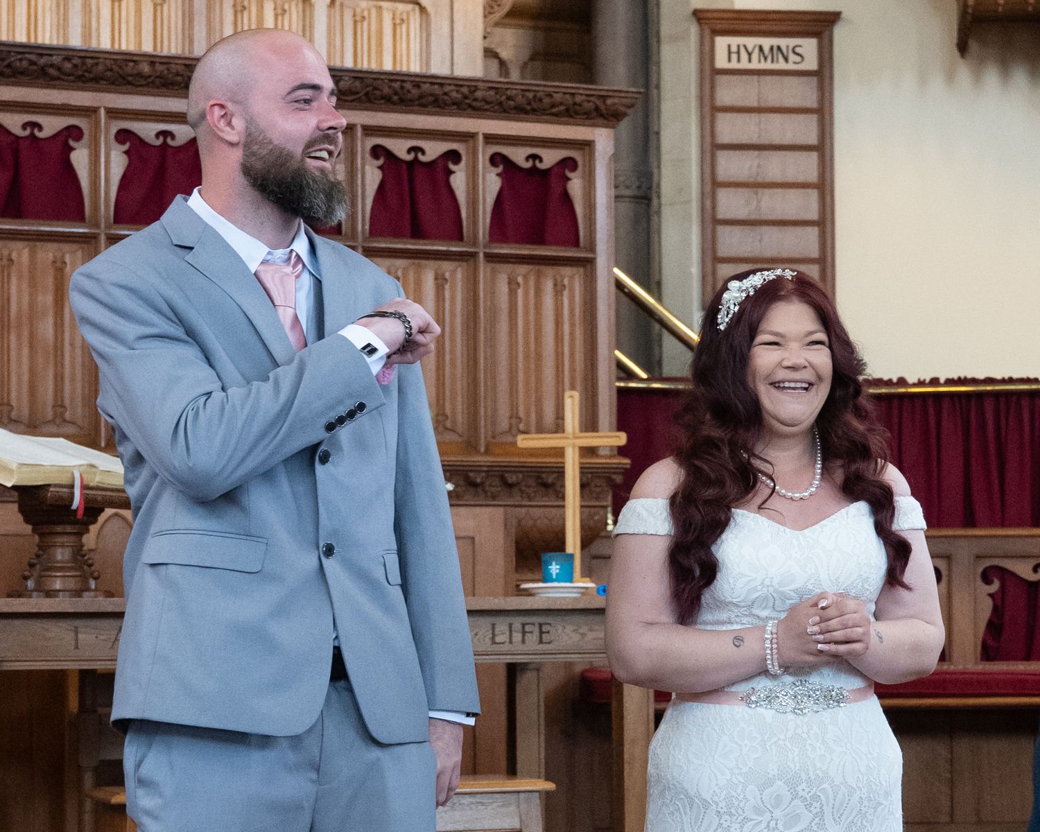 A couple embraces during their wedding ceremony in a church with wooden decor.