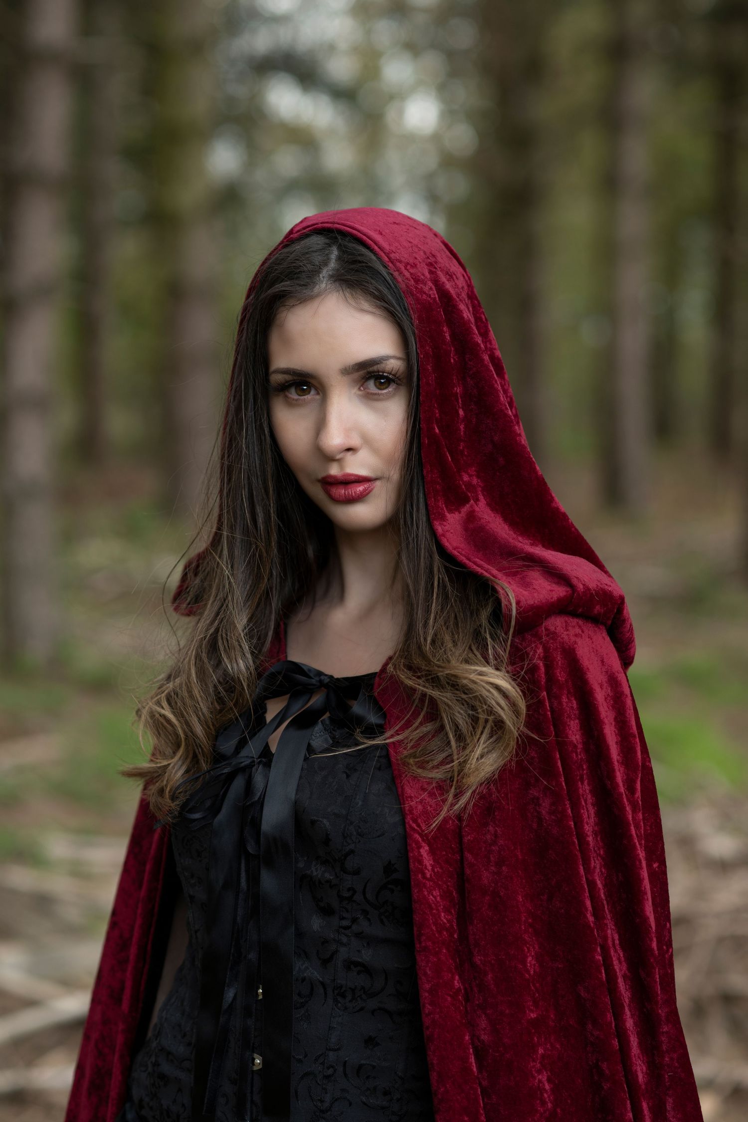 Dramatic portrait series of woman in red velvet cloak and black dress in forest setting.