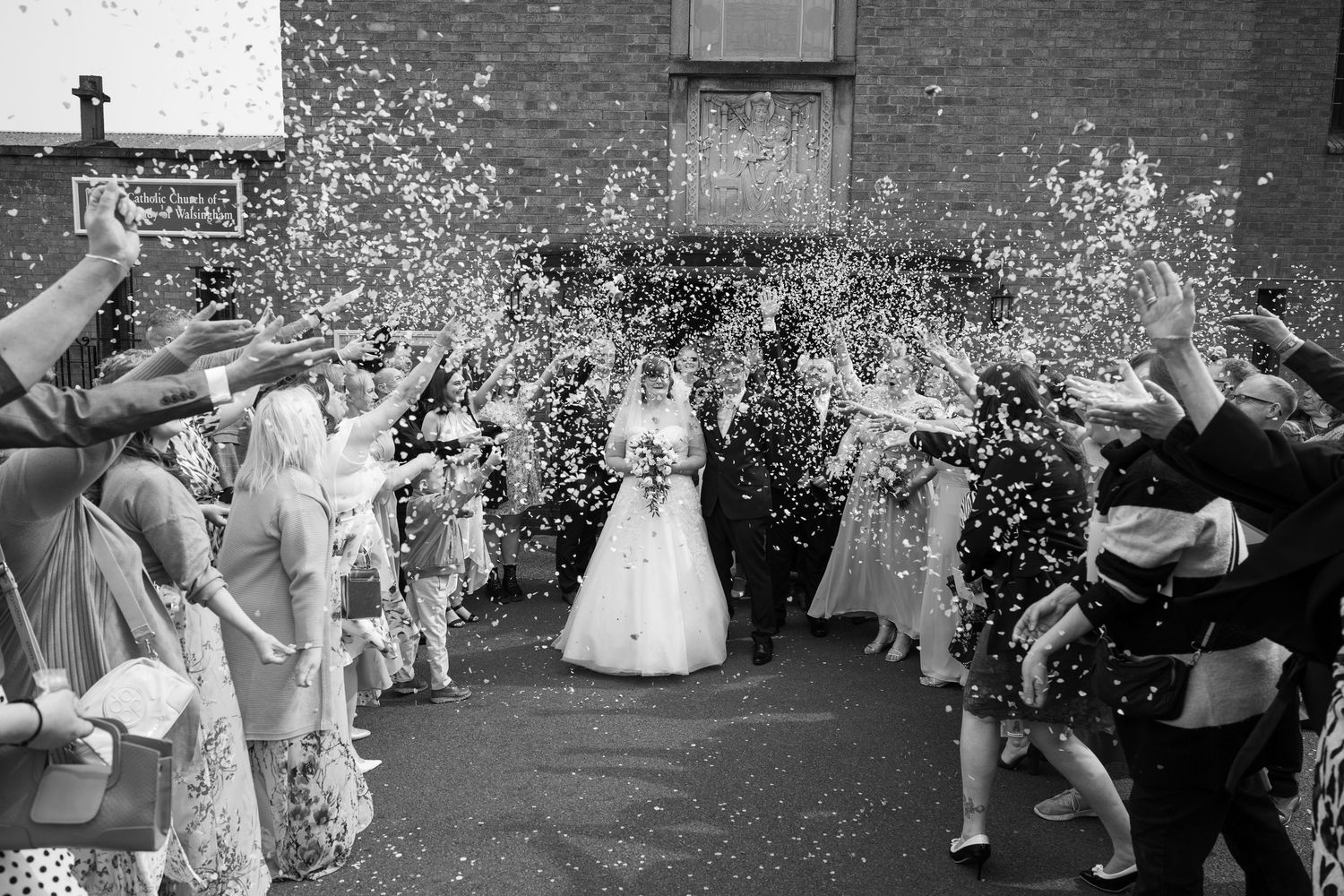 Black and white sequence of wedding guests throwing confetti outside.