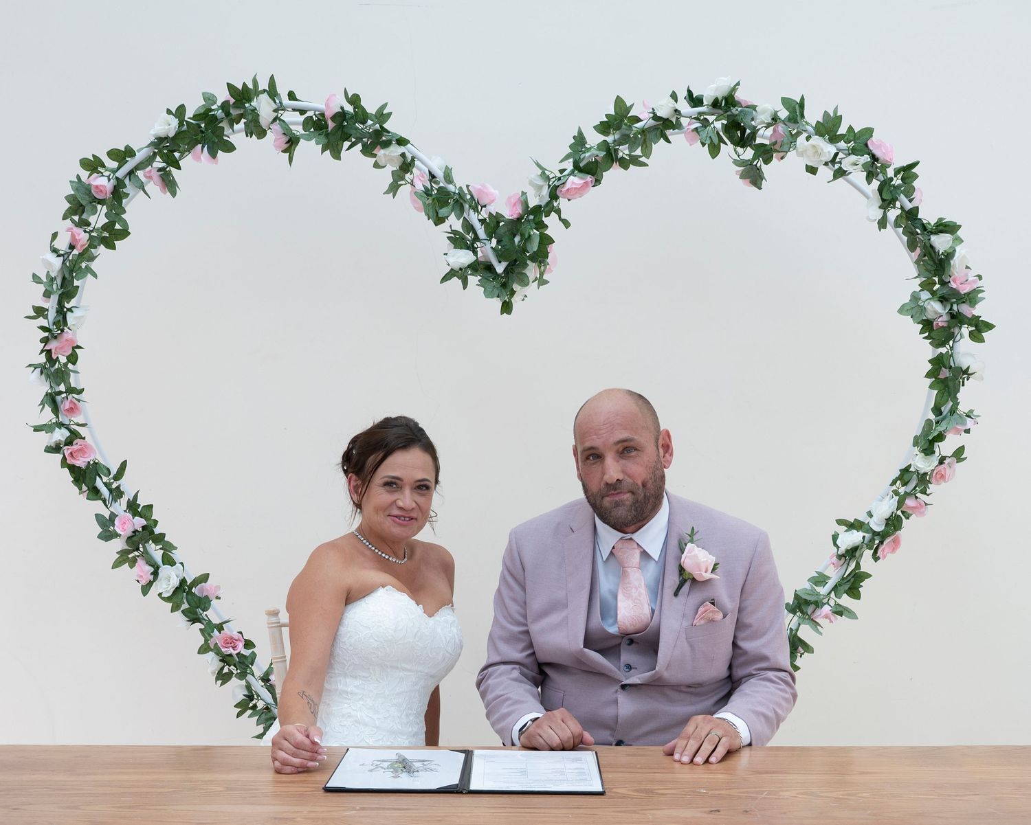 Wedding ceremony photos with floral arch decorations and signing moments at a white venue.