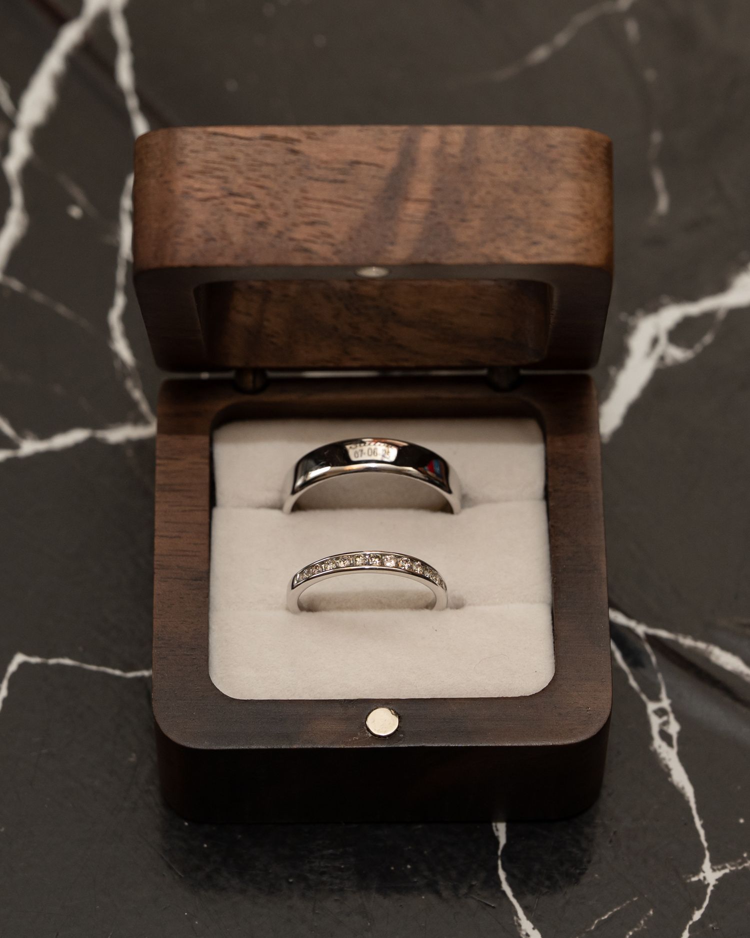 Diamond wedding rings displayed in wooden jewelry boxes on marble surface.