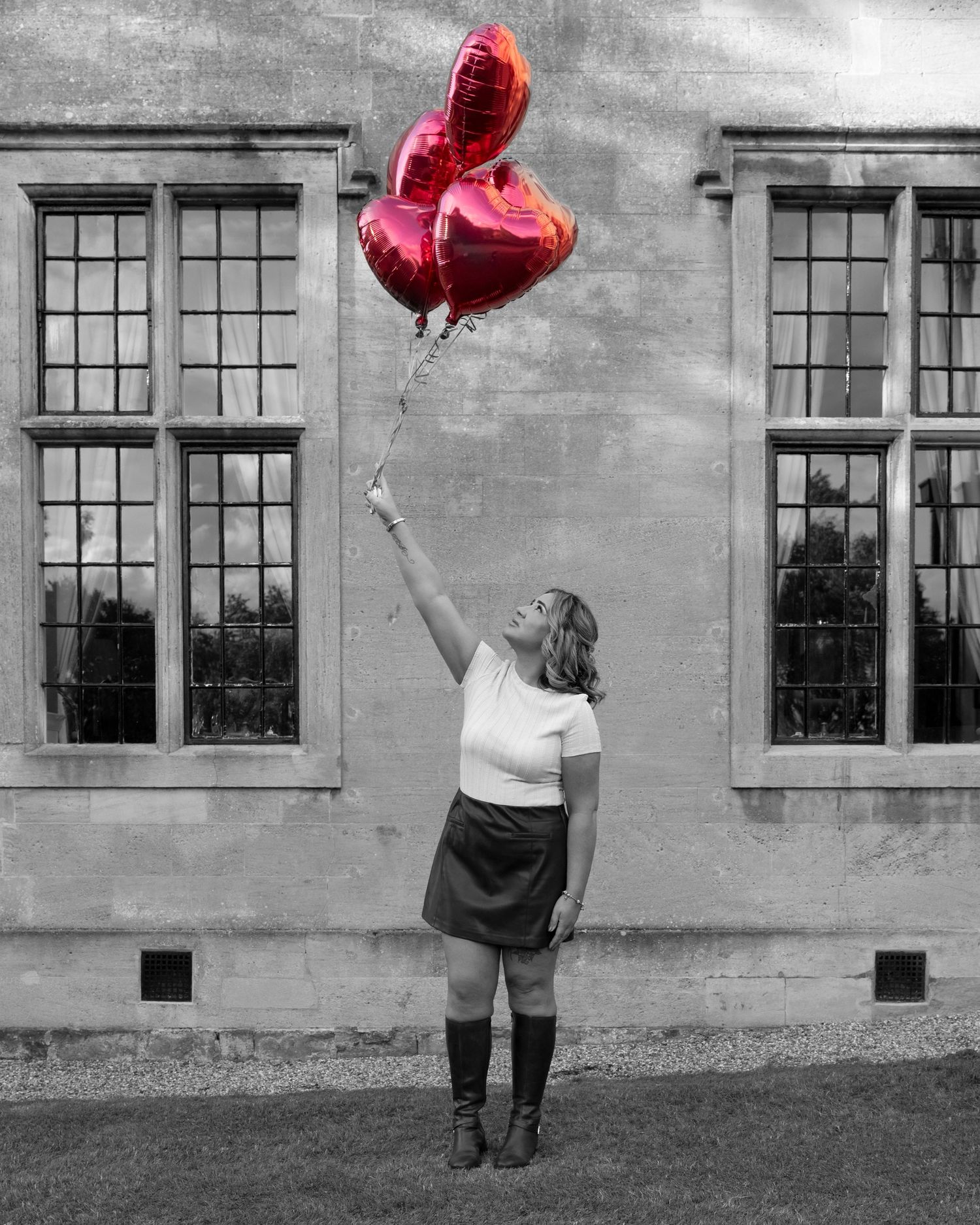 Black and white photos of a person with heart balloons in front of a building with large windows.