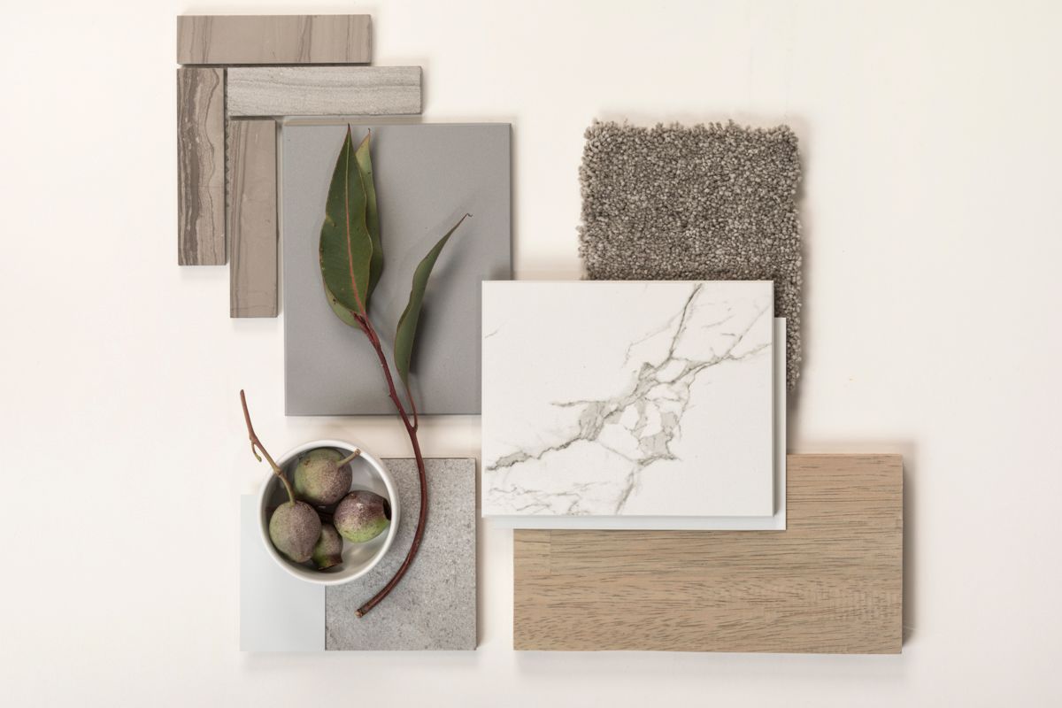 Flat lay of interior design material samples including marble, wood, stone, and carpet swatches with olive branch decor.