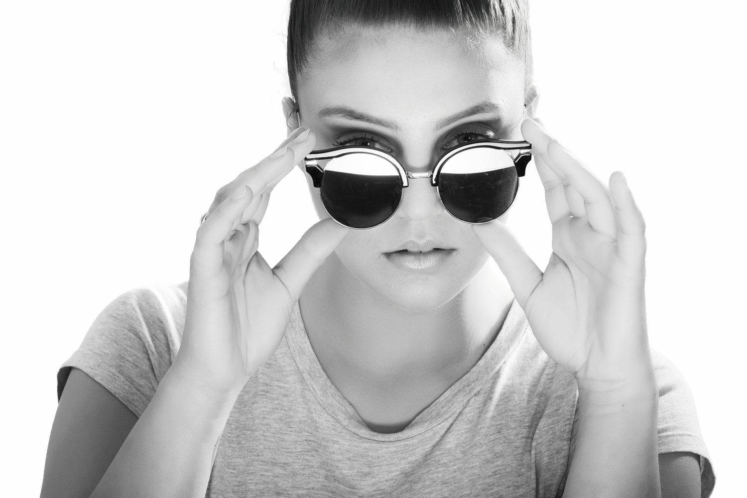 Stylish young woman in black and white photo adjusting trendy cat-eye sunglasses.