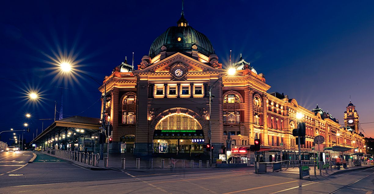 Flinders Street Station illuminated at night in Melbourne, Australia, showcasing its iconic Edwardian architecture and golden facade.