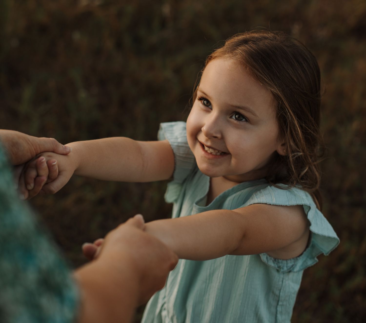 Young girl smiling while holding her mother's hands during an outdoor family photography session. Goodreau.co