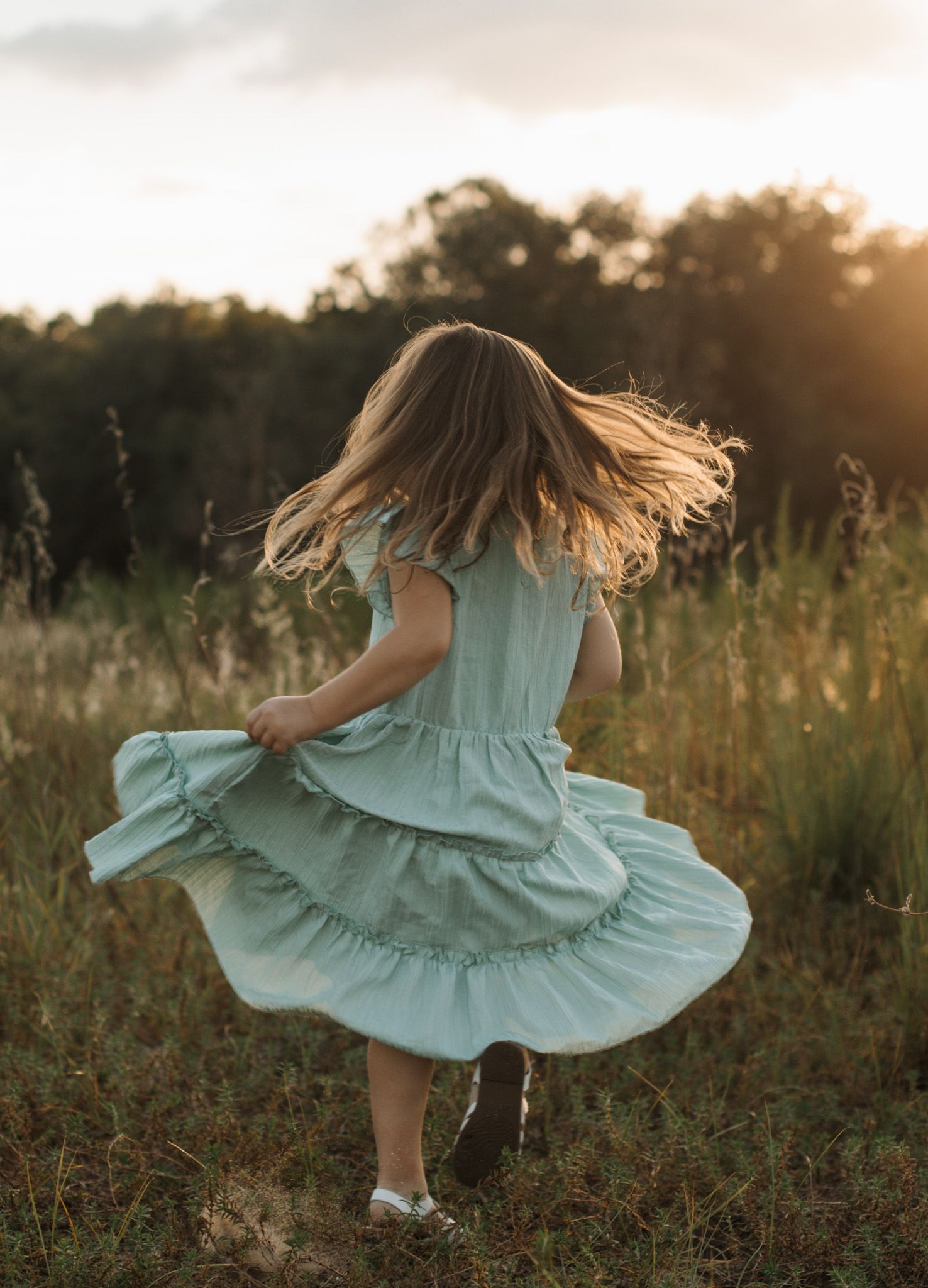 Young girl twirling her dress in a sunlit field during a candid lifestyle photography session. Goodreau.co