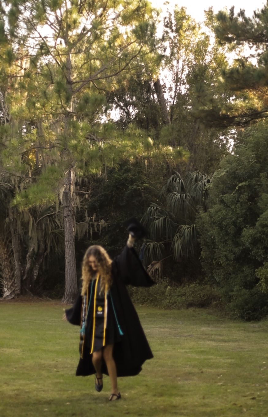 UCF graduate walking through a field in cap and gown during a graduation photography session. Goodreau.co