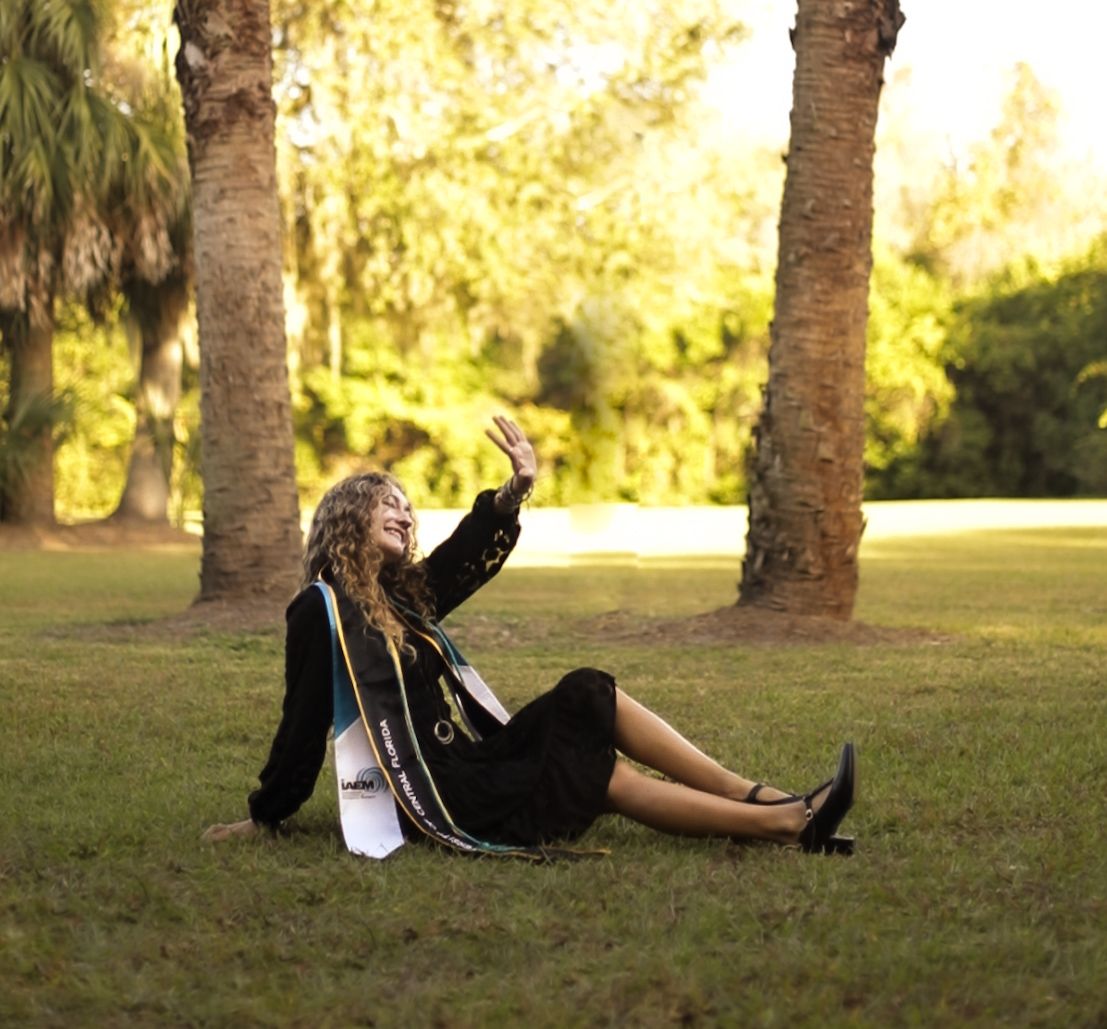 UCF graduate sitting beneath palm trees during an outdoor graduation photography session. Goodreau.co