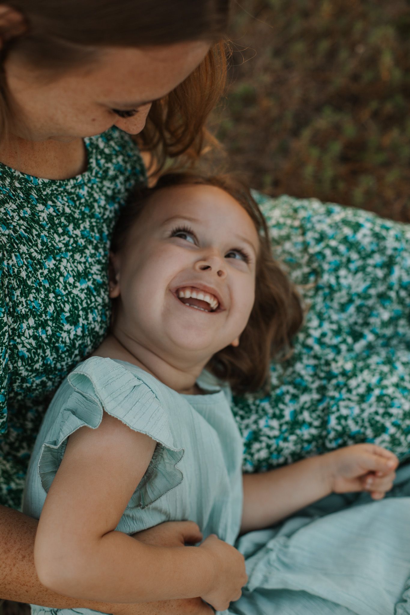 Young daughter smiling up at her mother during a candid lifestyle family session. Goodreau.co