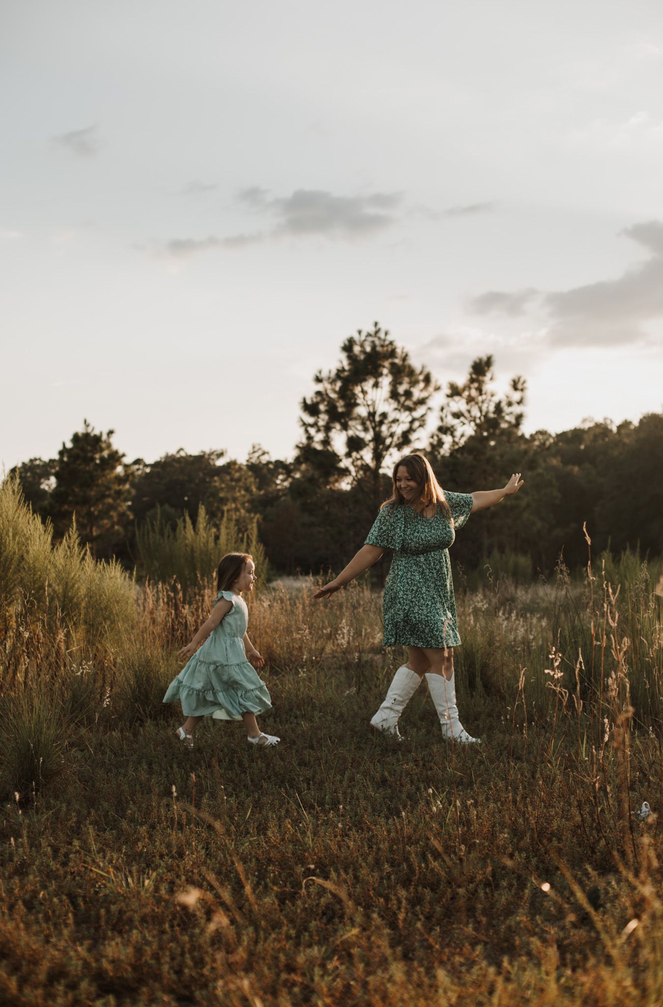 Mother and young daughter holding hands and playing in a field at golden hour. Goodreau.co