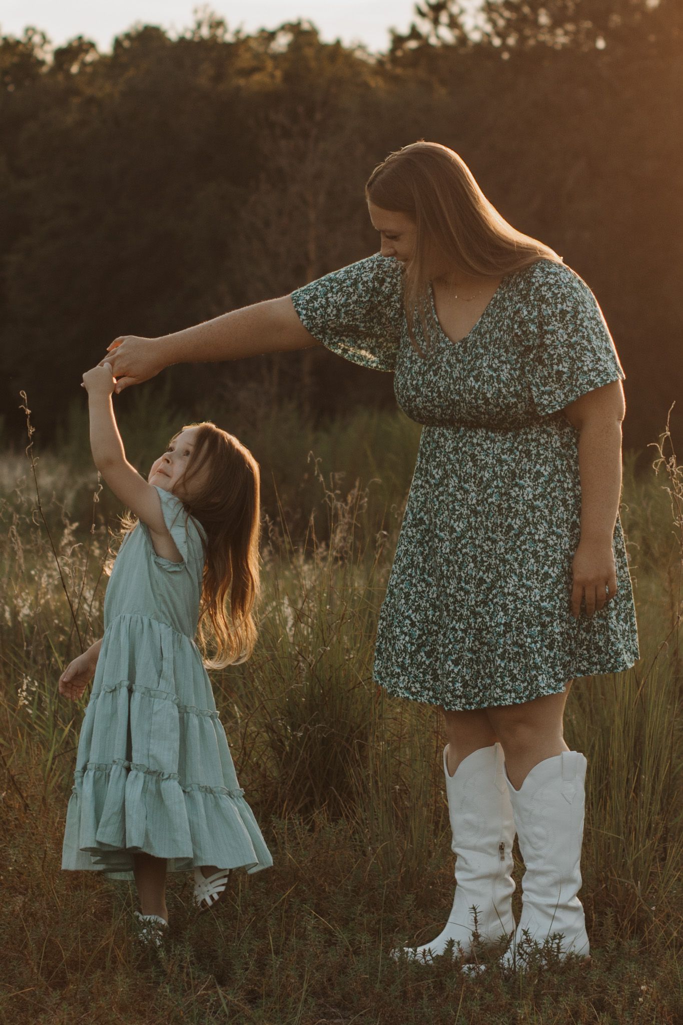 Mother and daughter dancing together in a sunlit field during a lifestyle family session. Goodreau.co