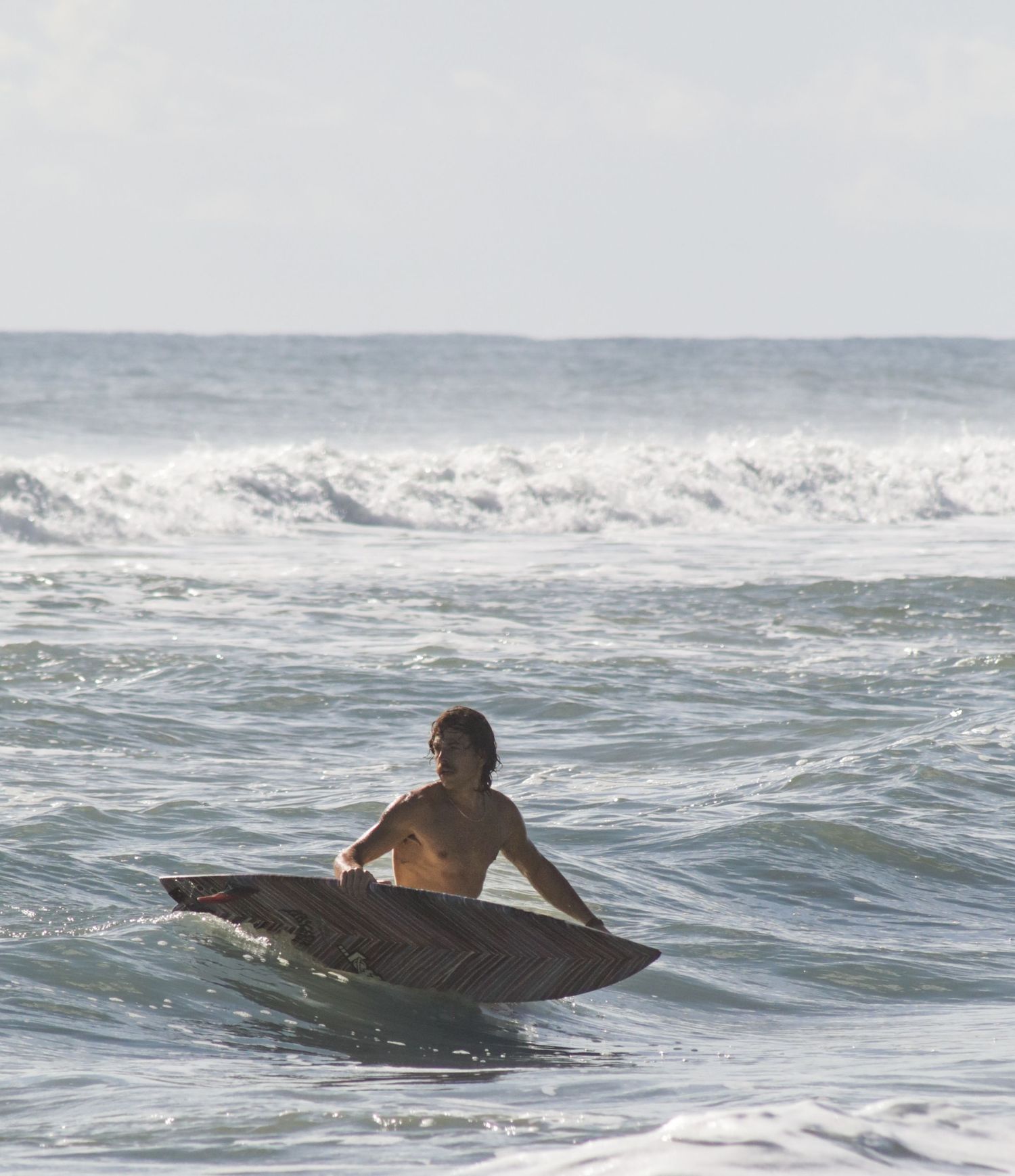 Surfer carrying a surfboard through ocean waves during a Florida surf photography session. Goodreau.co