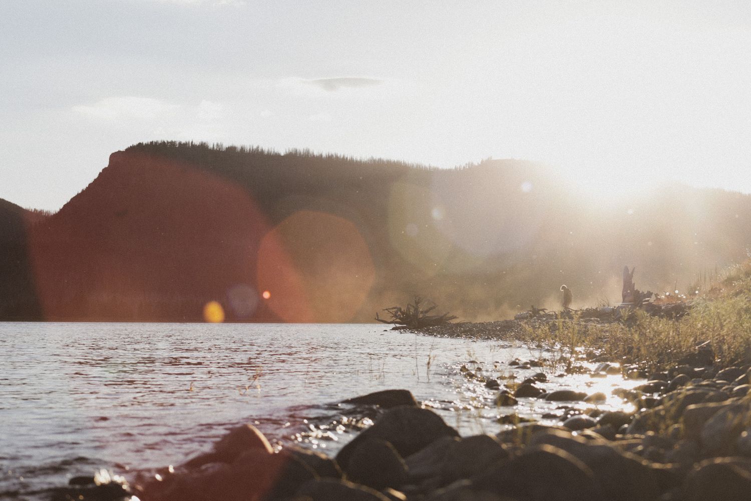 Sunlight over a rocky shoreline and water captured in a warm documentary style. Grand Teton National Park. Goodreau.co