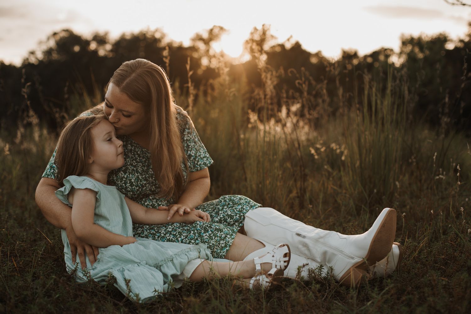 Mother and daughter cuddling together in a field during a golden hour family photography session. Goodreau.co