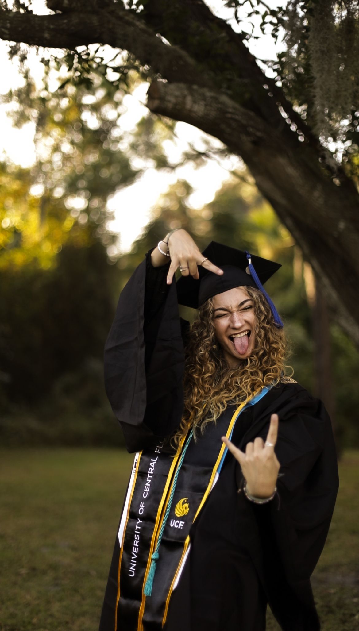 UCF graduate posing playfully in cap and gown during an outdoor graduation portrait session. Goodreau.co