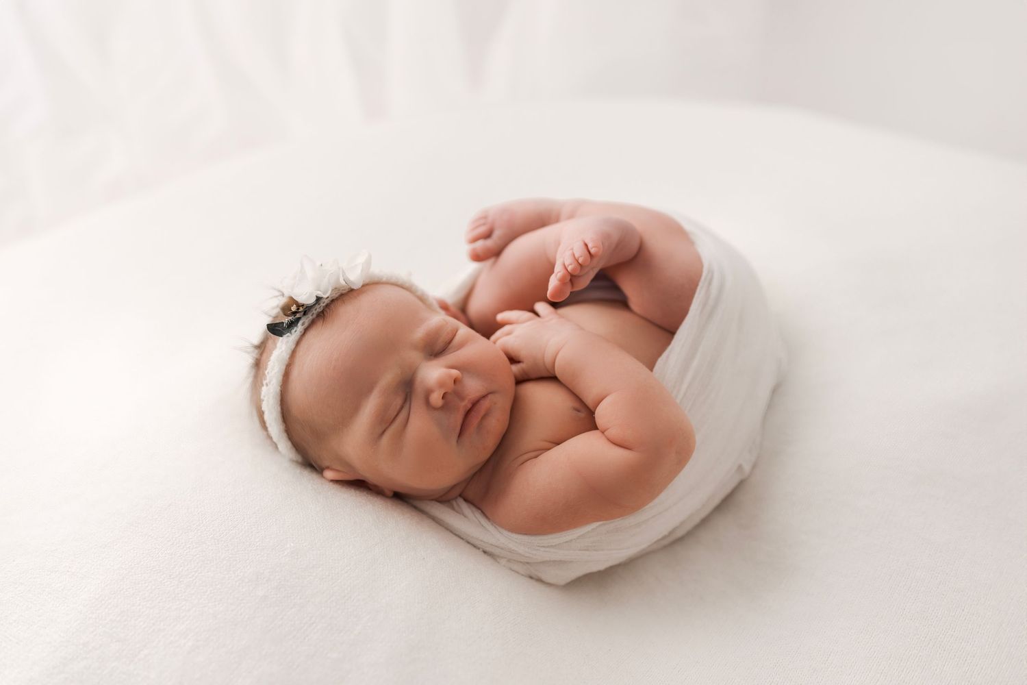 Peaceful newborn baby girl wrapped in white swaddle sleeping on soft white blanket.