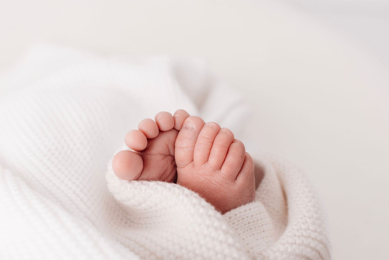 Close-up of tiny newborn baby feet peeking out from a soft white knit blanket.