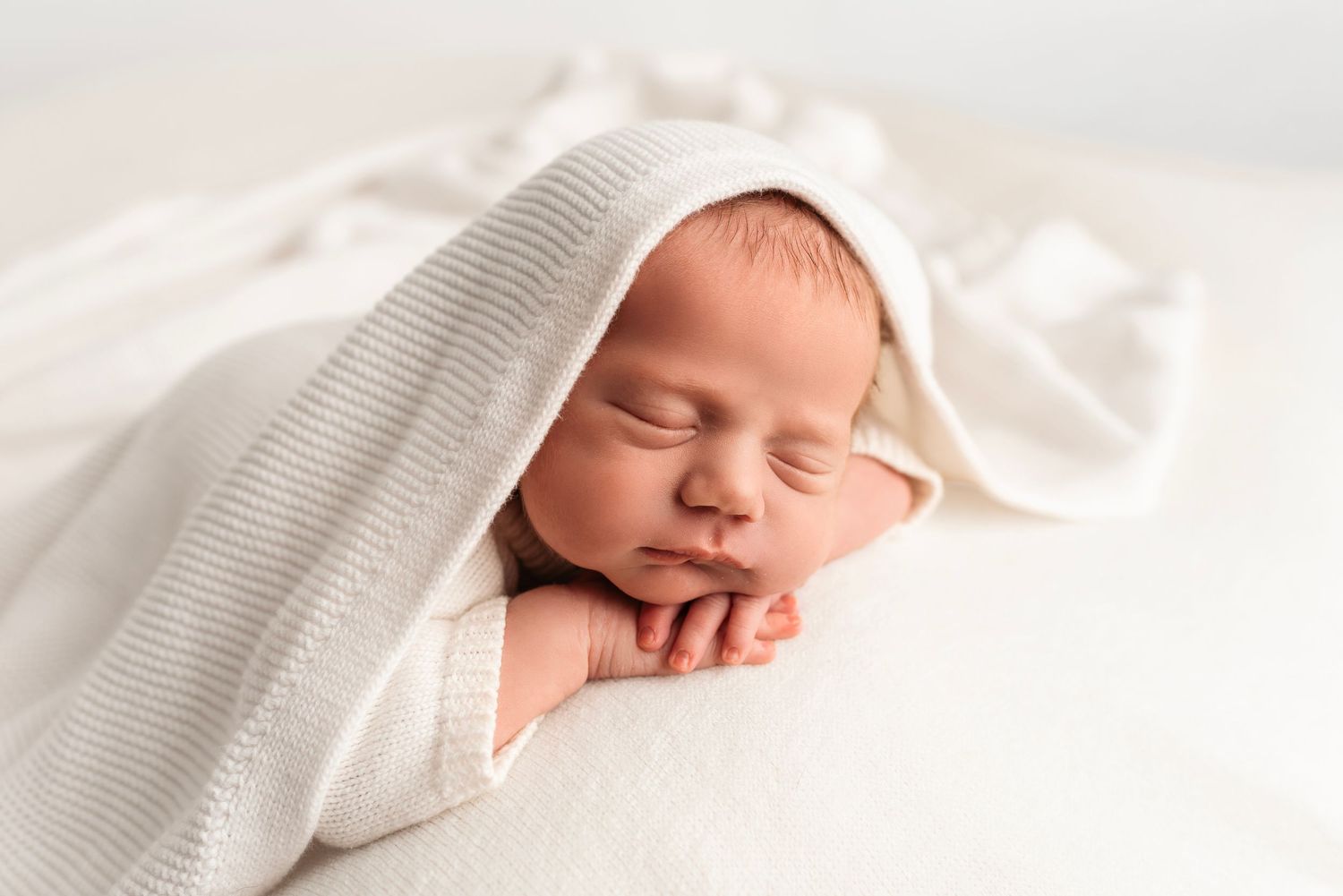 Serene newborn baby sleeps peacefully under a soft striped white blanket in a studio photo.