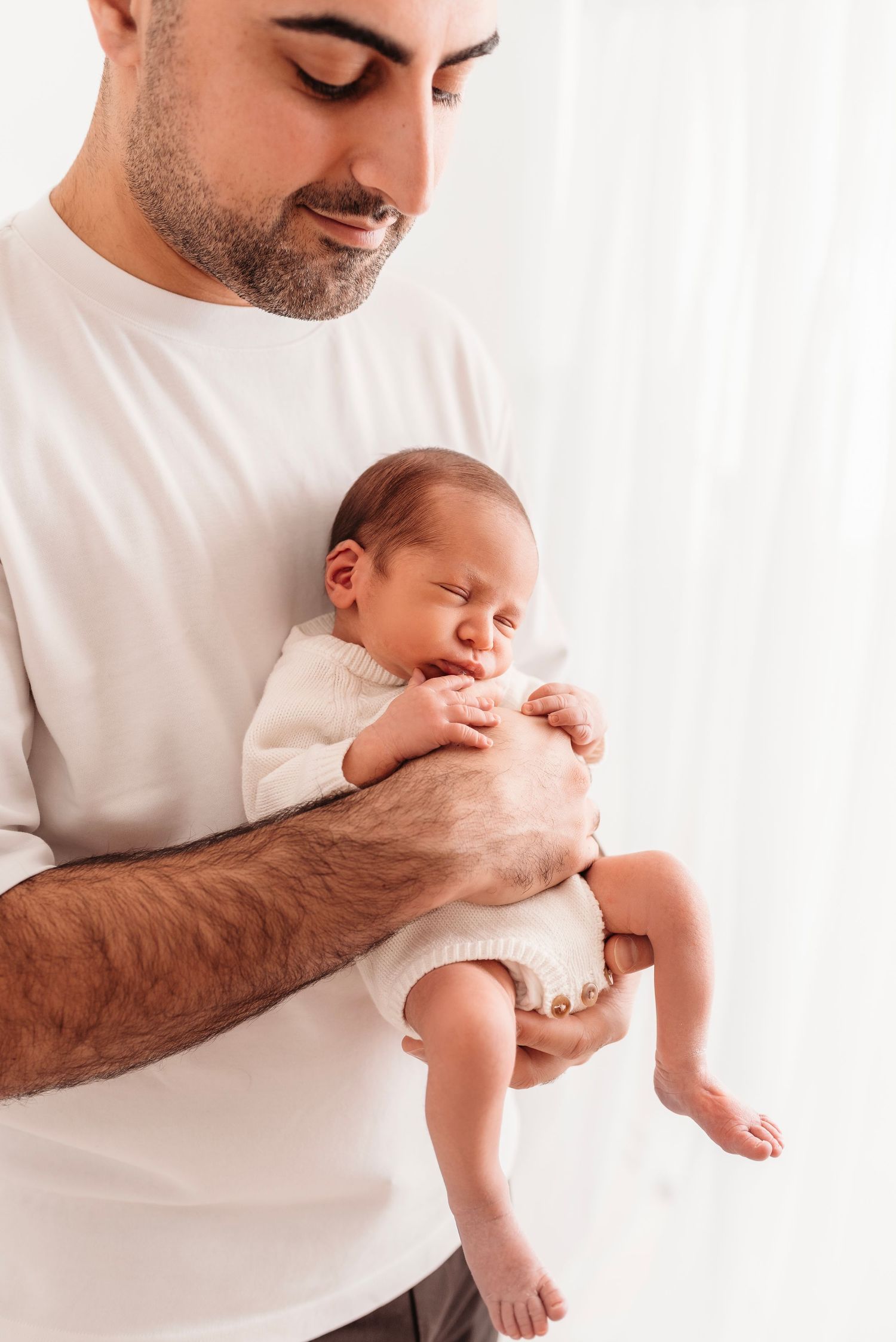 Loving father in white shirt gently cradling his sleeping newborn baby in his arms.