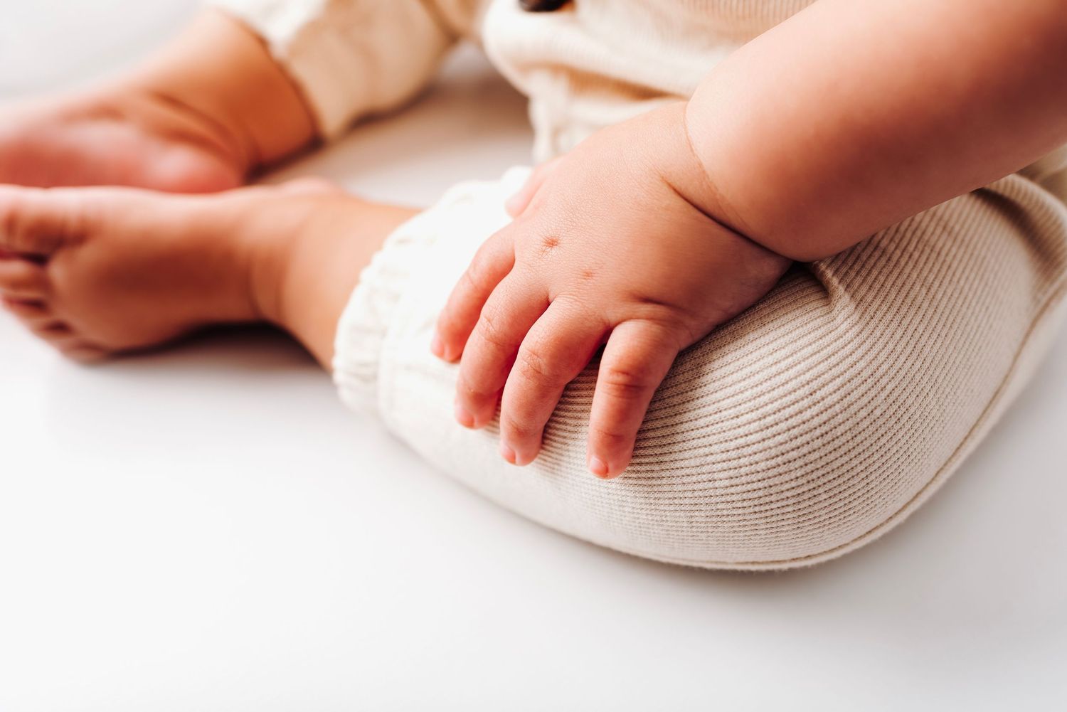 Close-up of cute baby hands and feet resting on soft beige fabric.