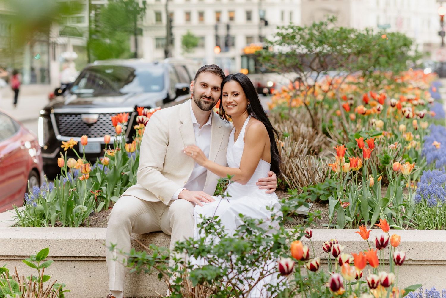 Happy couple embraces while seated among bright tulips with Chicago urban streetscape in background.