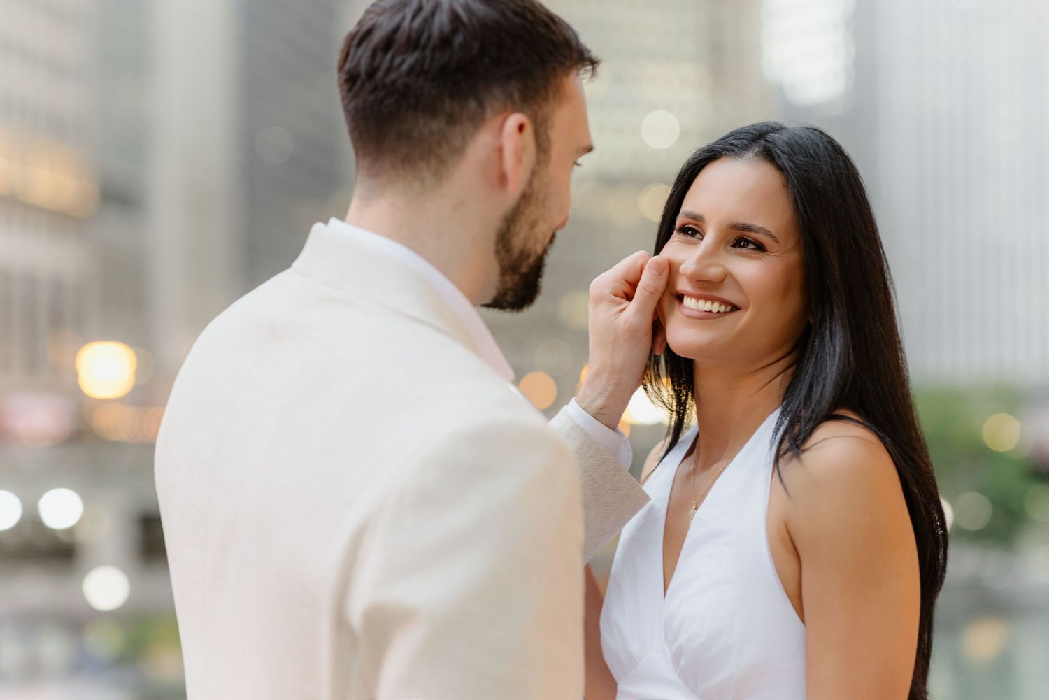 Man in white suit gently touching smiling woman's face during romantic Chicago engagement photo session.