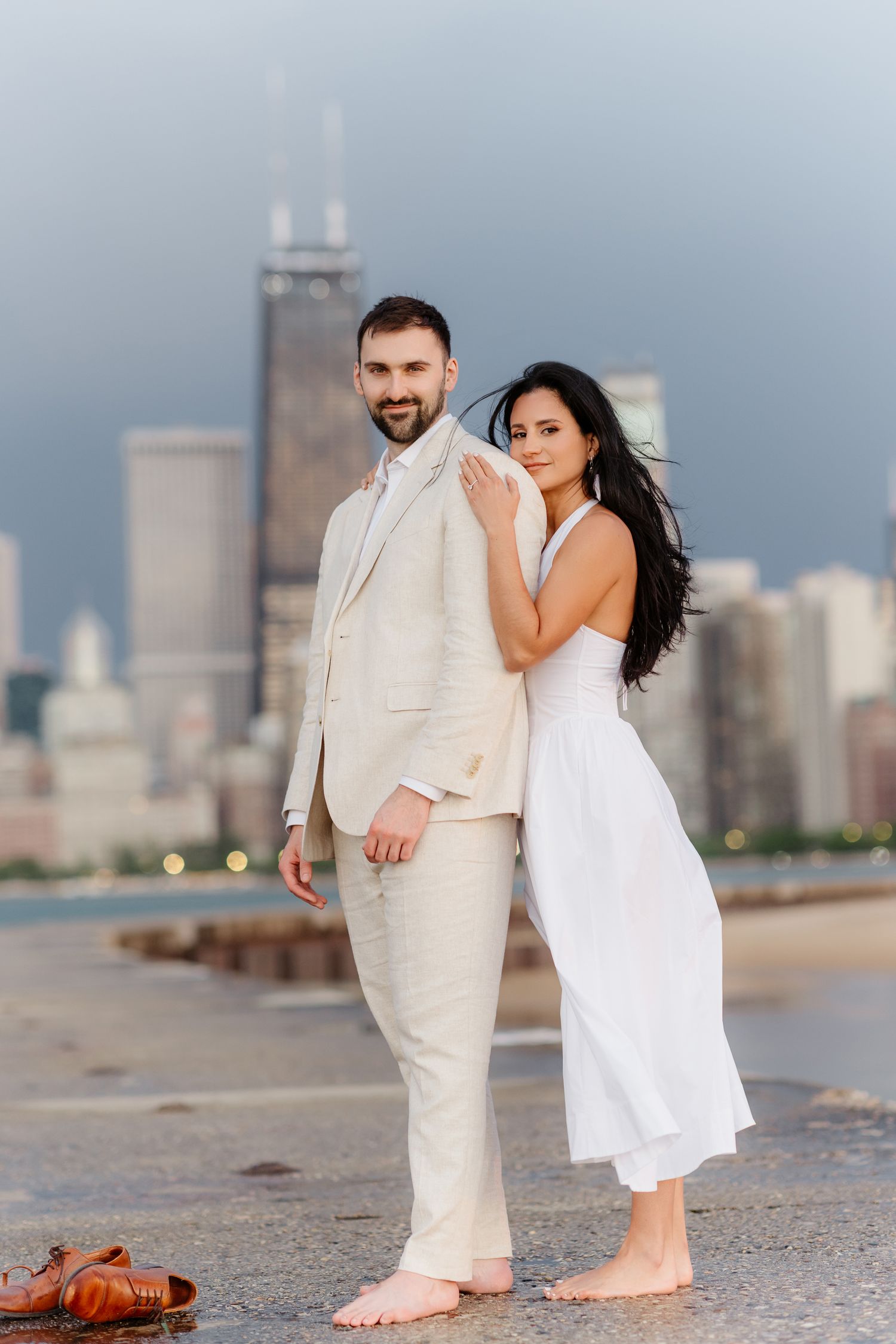Barefoot couple standing back-to-front on Chicago lakefront pier with John Hancock Tower in background.