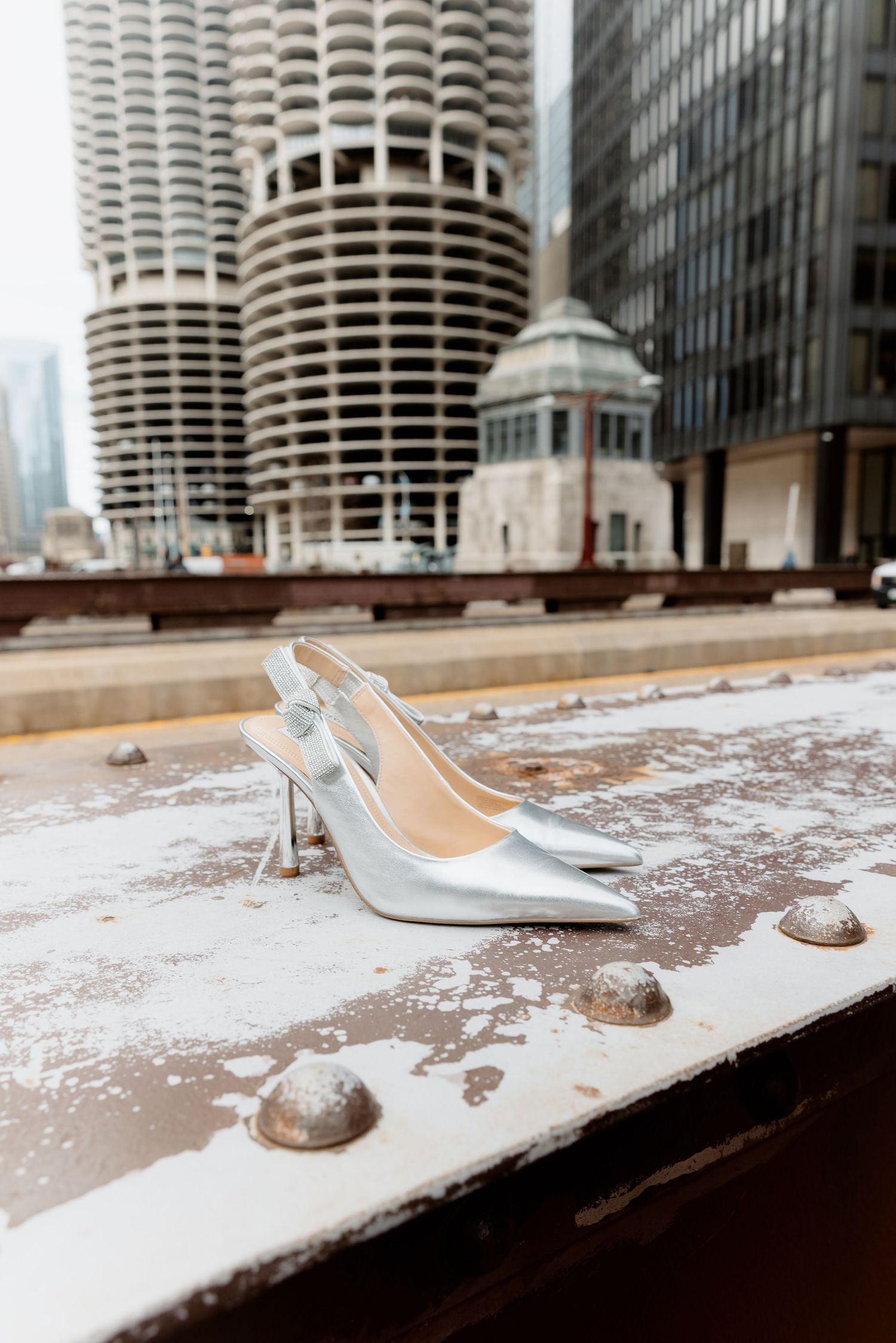 Silver slingback stiletto heels placed on a weathered ledge with iconic Marina City towers in Chicago backdrop.