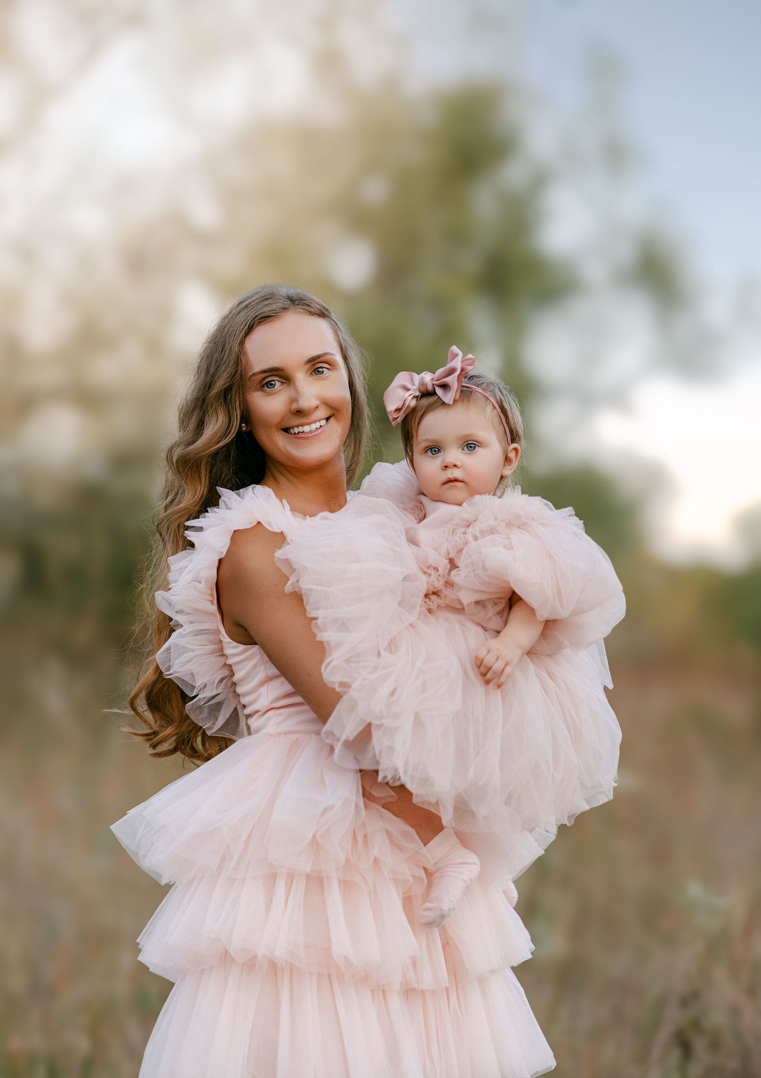 Mother and baby girl in matching pink ruffle tulle dresses posing outdoors at golden hour.