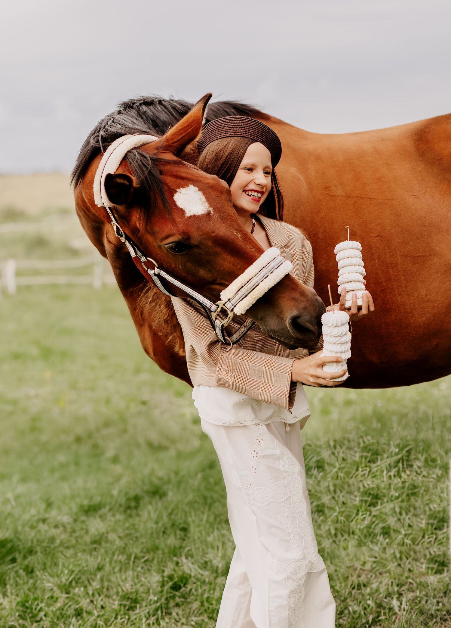 Smiling girl in white pants embracing a chestnut horse outdoors on a farm.