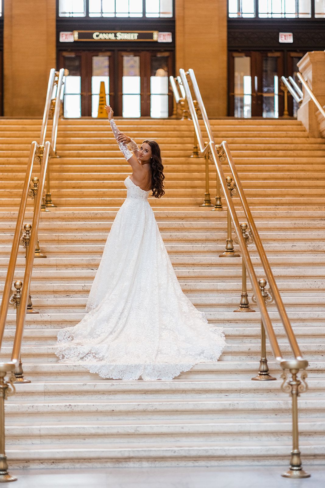 Bride in white lace gown with train poses on grand staircase at Canal Street station.