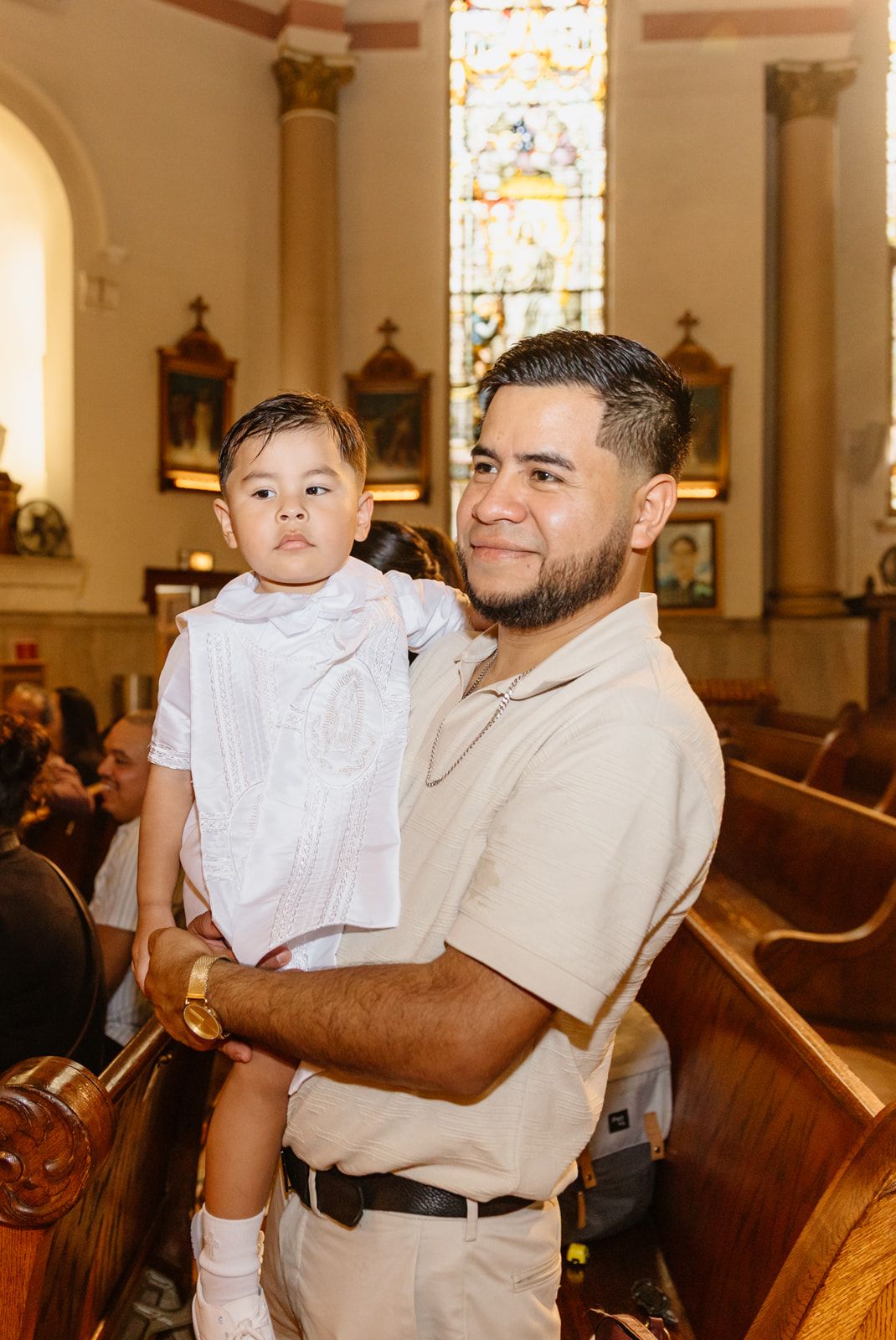 Smiling father holding his son dressed in white at a Catholic baptism ceremony.