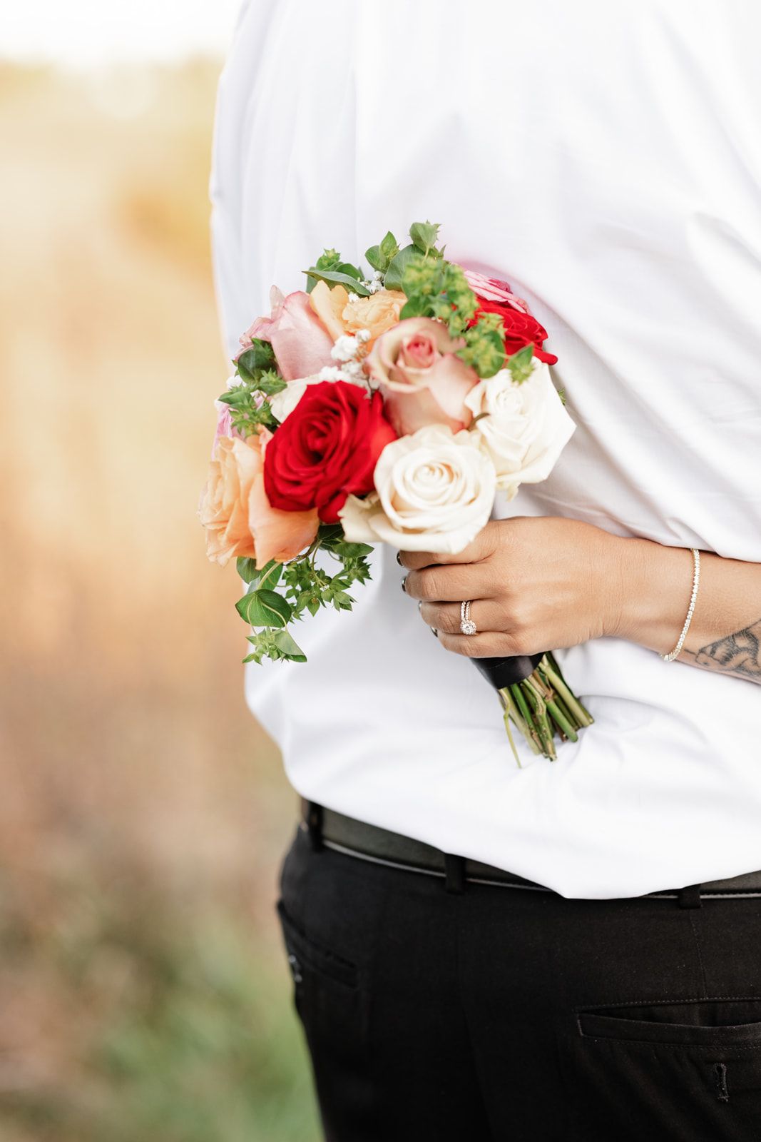 Bride holding a colorful wedding bouquet of red, pink, and white roses against a groom in a white shirt.