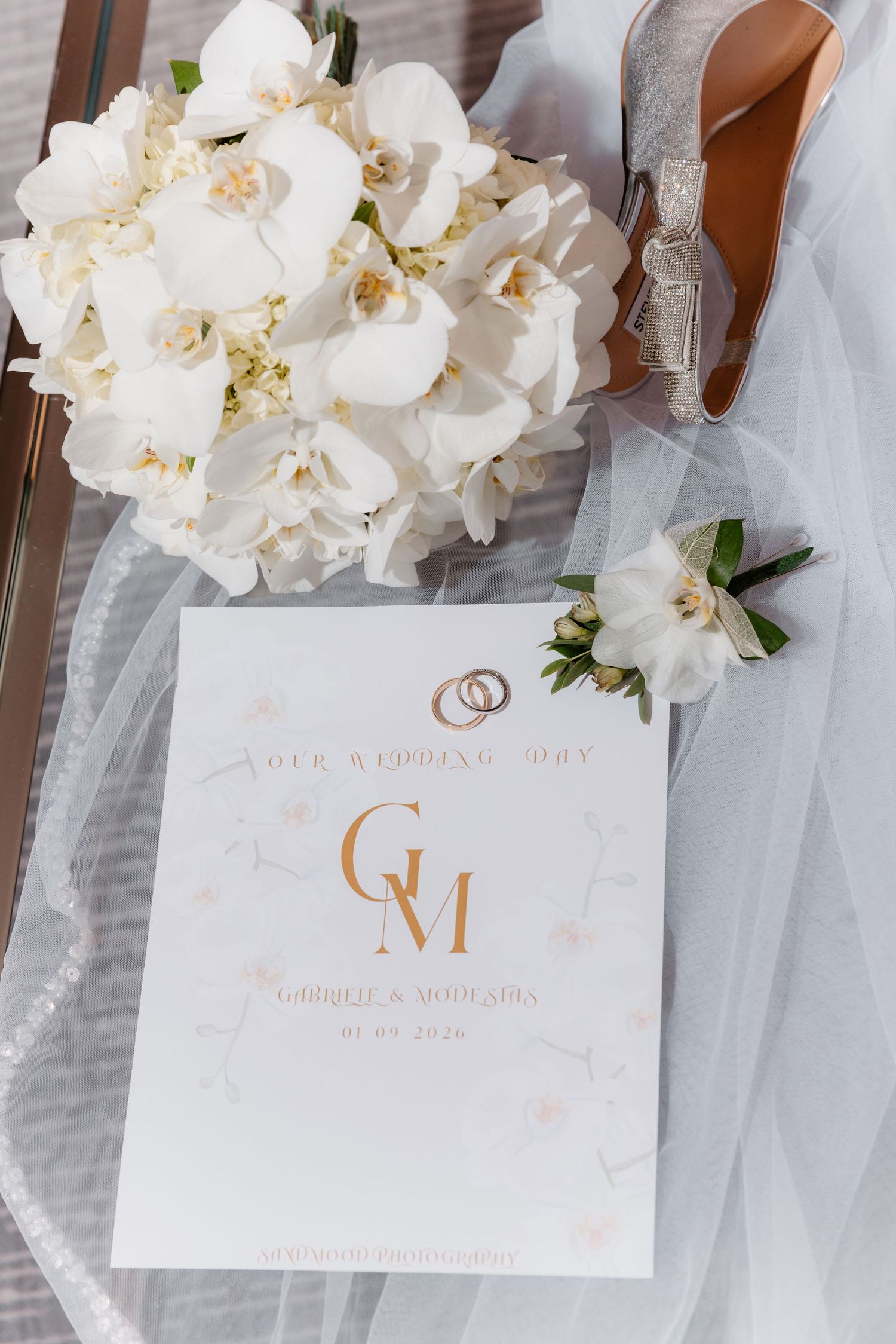 Wedding flat lay featuring white orchid bouquet, gold rings, boutonniere, silver heels, and monogrammed GM wedding program.