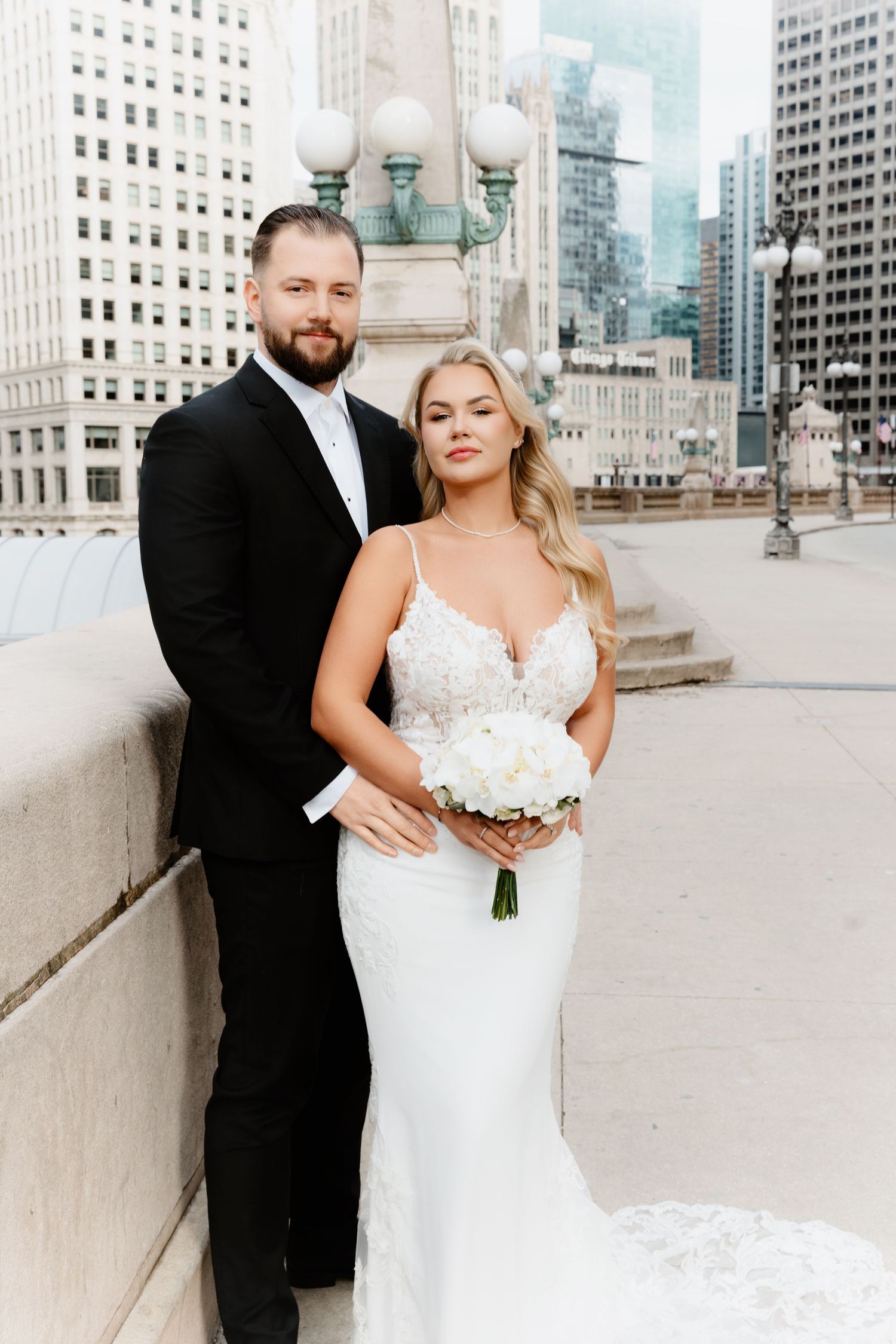 Bride holding white floral bouquet and groom embrace on Chicago Wabash Bridge with skyscrapers behind them.