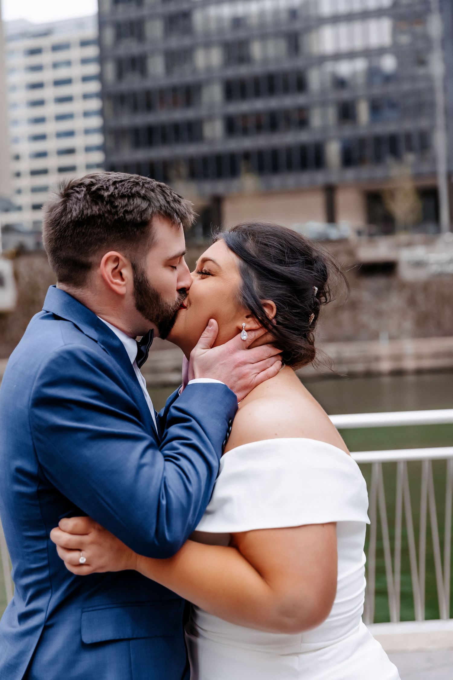 Bride and groom share first kiss in blue suit and white off-shoulder gown on Chicago Riverwalk.
