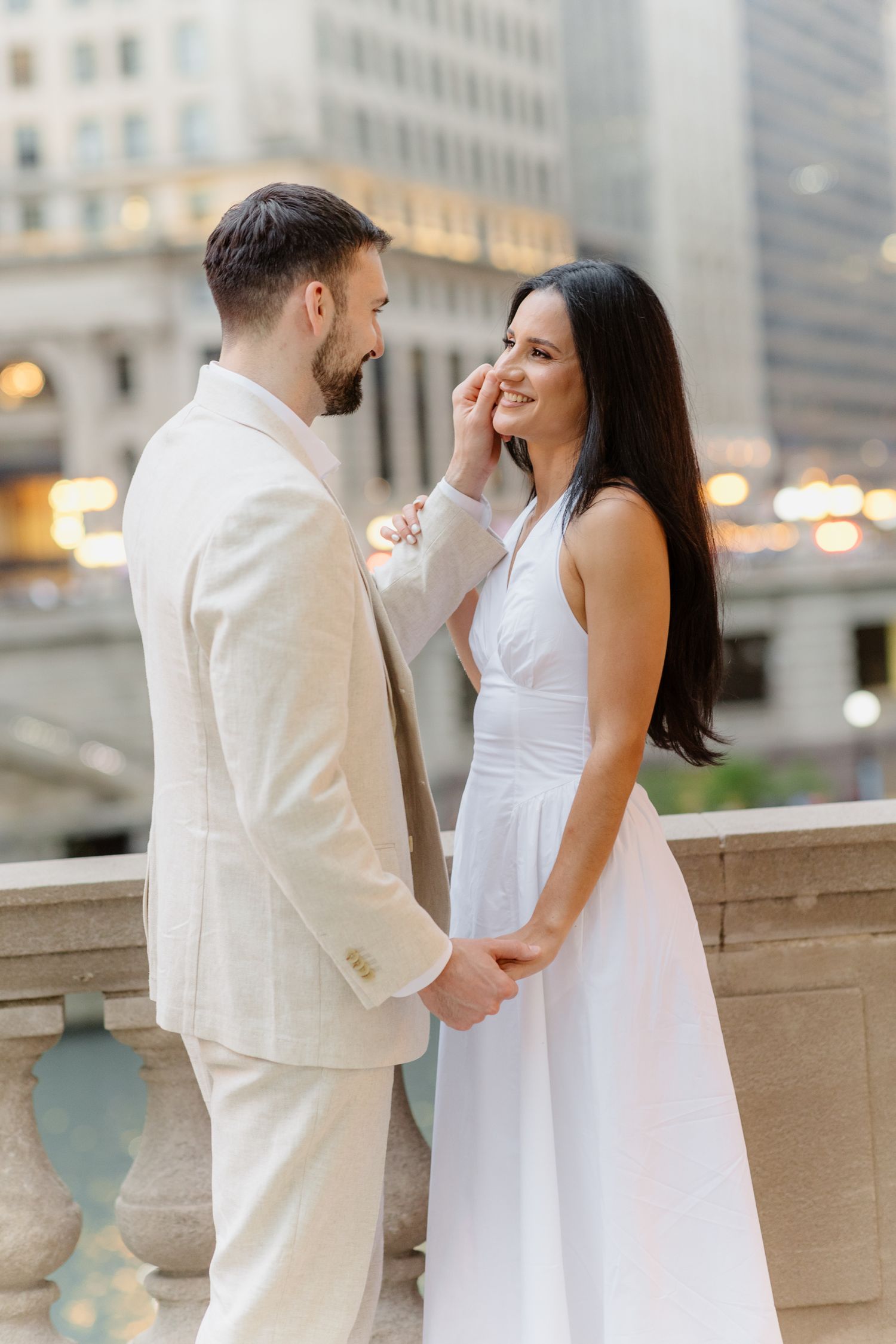 Couple laughing and holding hands on Chicago riverwalk balcony with glowing city lights in background.
