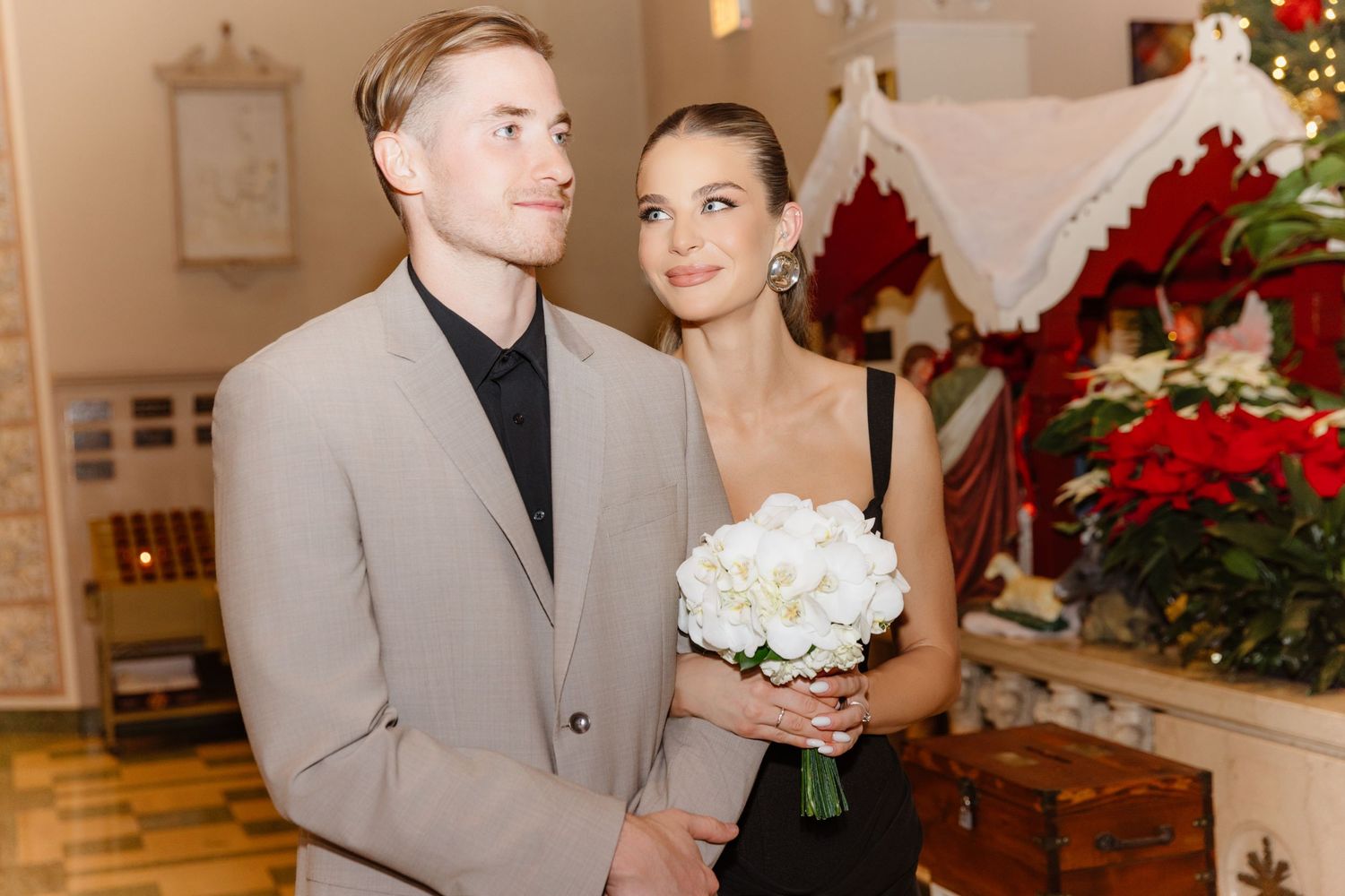 Bride in black dress holding white bouquet with groom in beige suit at Christmas wedding.