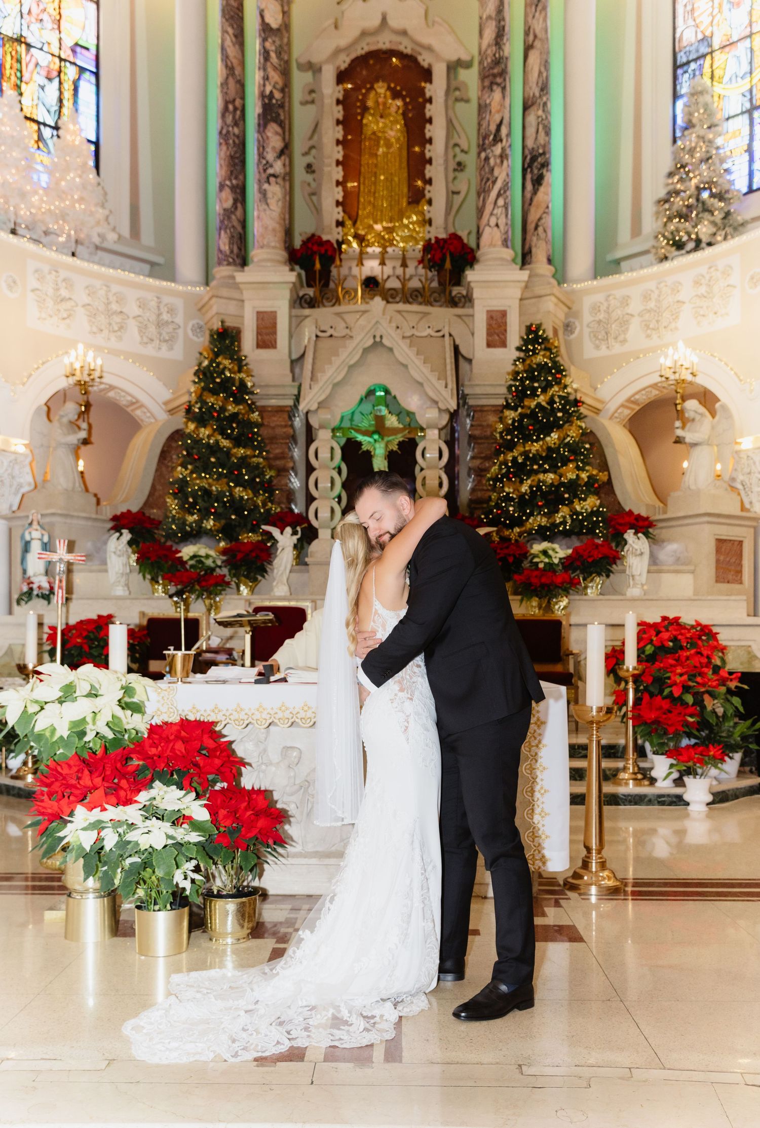 Couple embracing before elaborately decorated Christmas altar with poinsettias during winter wedding ceremony.