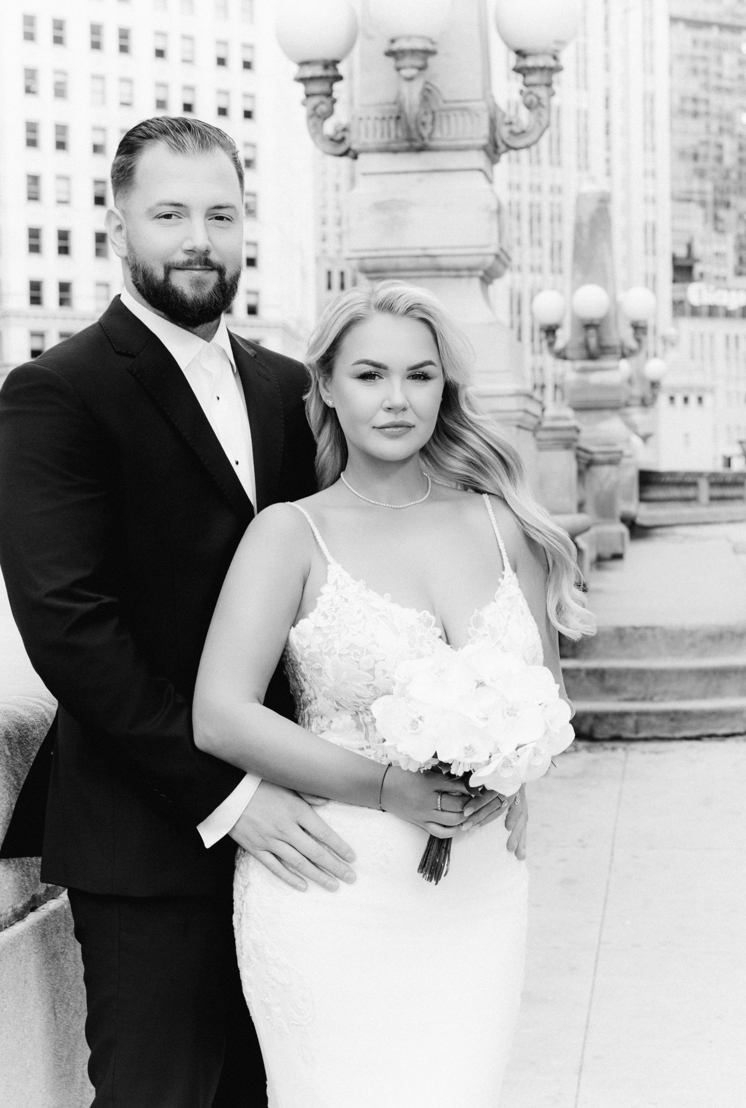 Black and white wedding portrait of blonde bride holding white bouquet with groom on Chicago bridge.