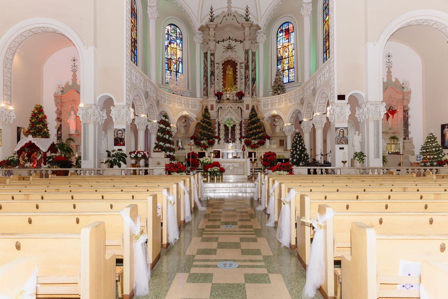 Beautifully decorated church interior with Christmas trees, poinsettias, and white pews for a wedding.