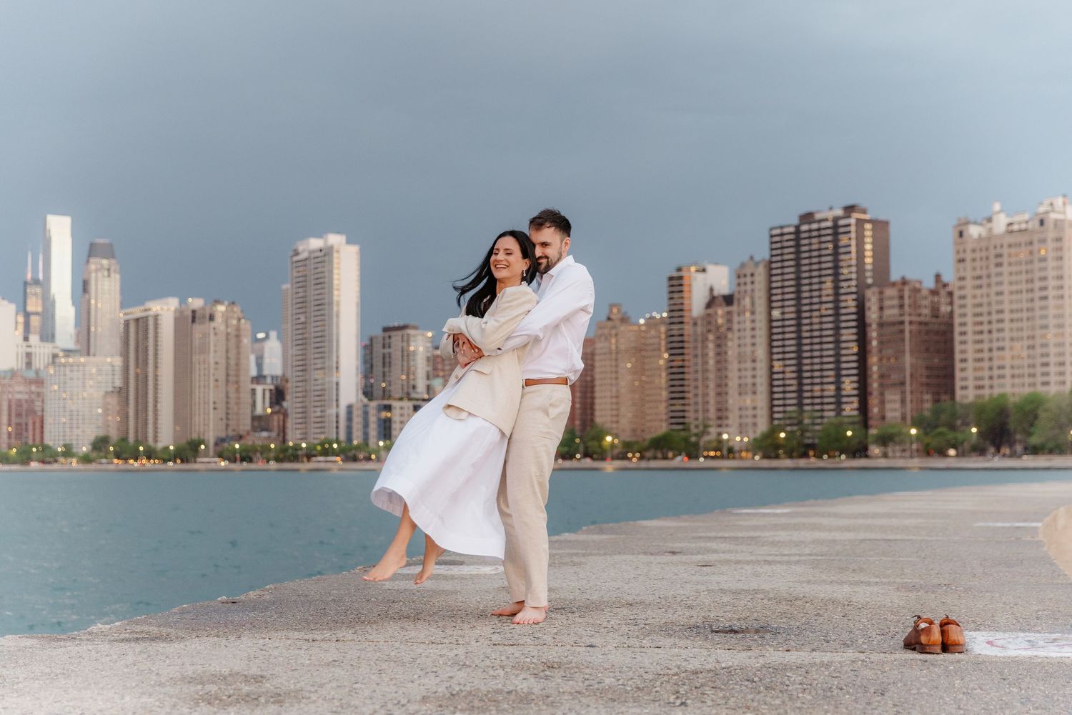 Happy couple dancing together barefoot on Chicago pier with iconic city skyline backdrop.