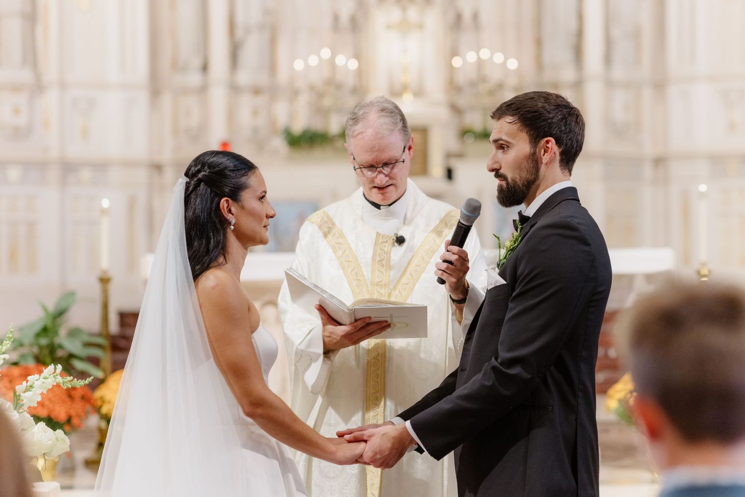 Bride and groom exchange vows holding hands before officiant at elegant church altar.
