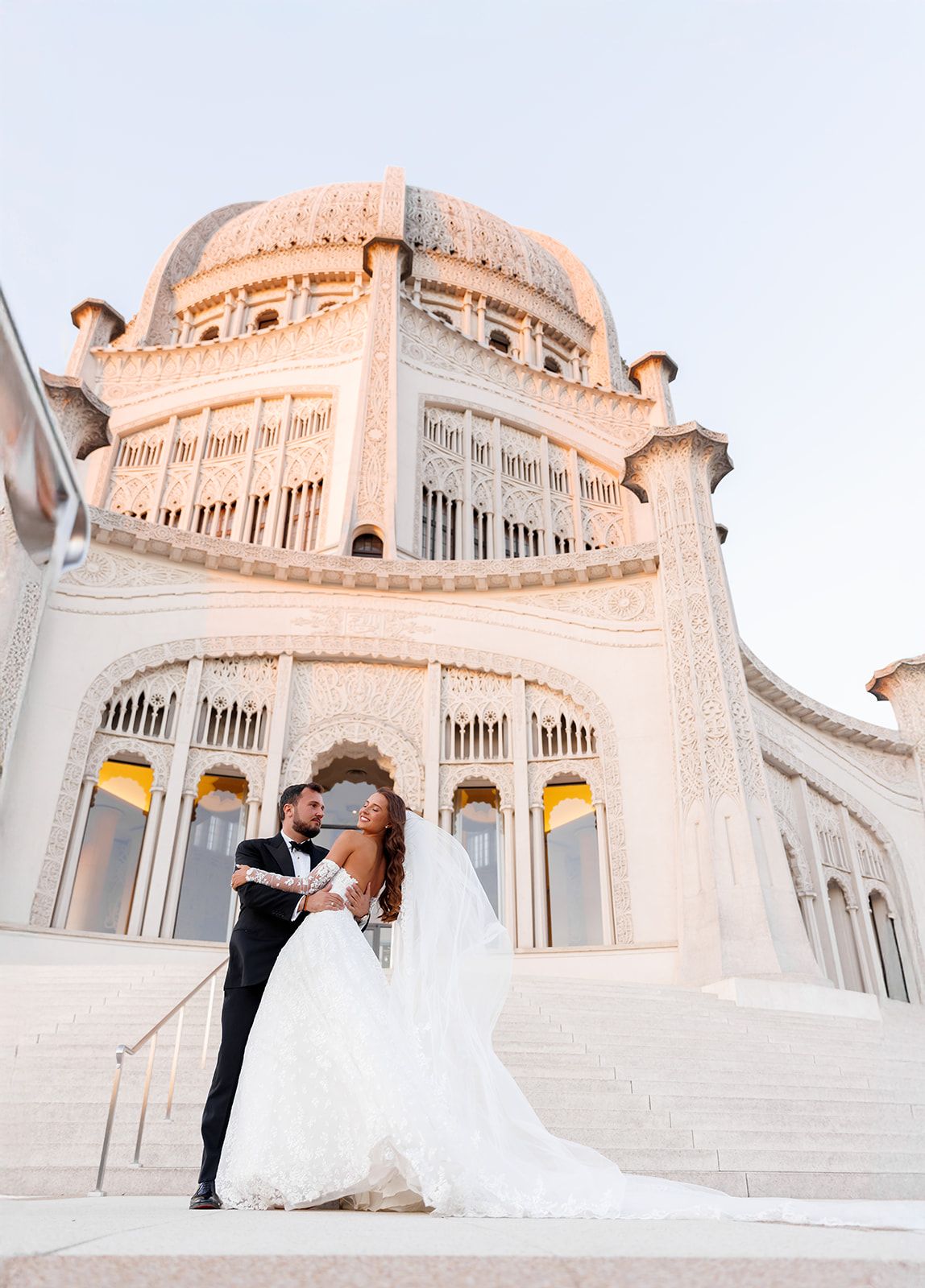 Wedding couple kissing at sunset before ornate Bahai Temple dome architecture.