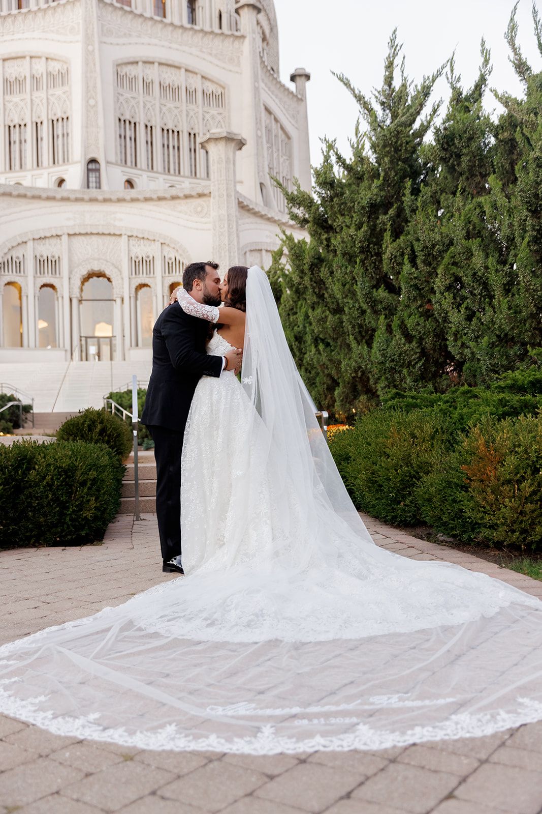 Bride and groom kissing in front of the Bahai Temple, showcasing her stunning cathedral lace veil.