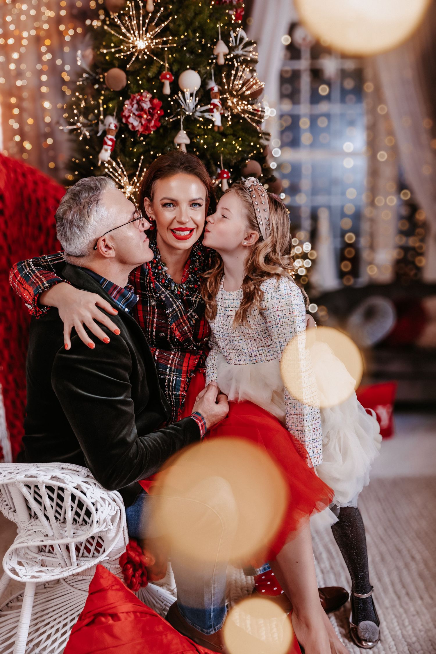 Family portrait with parents and daughter sharing kisses by decorated Christmas tree.